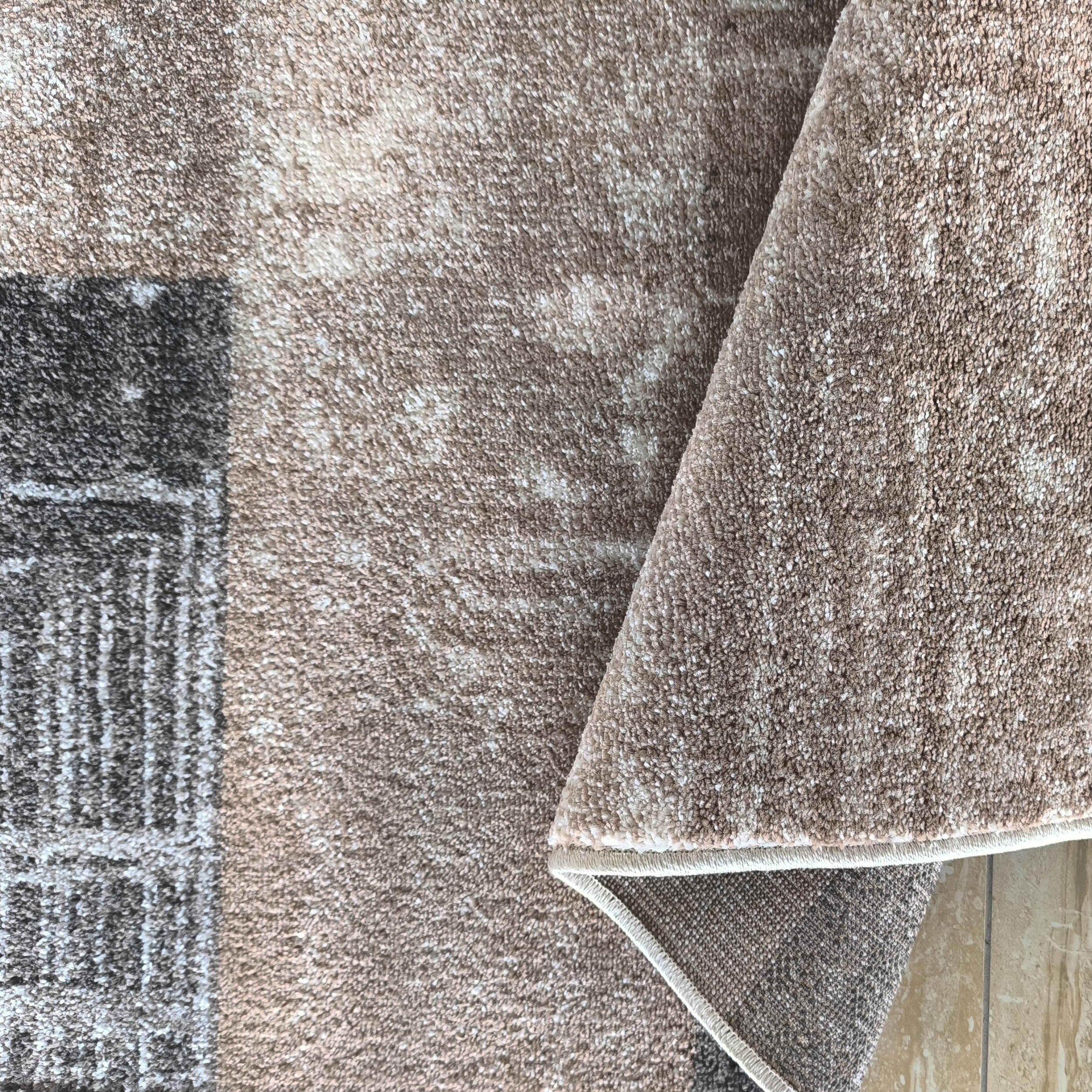 Tapis texturé beige et blanc à motifs rectangulaires gris foncé, replié sur son envers tissé et le carrelage beige