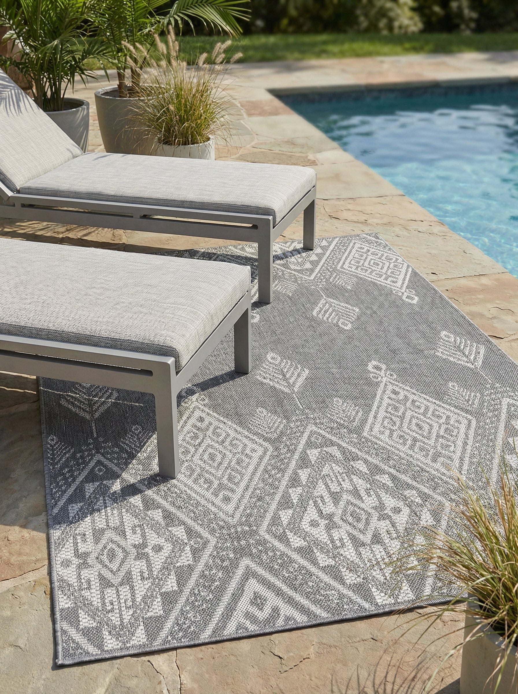 Tapis rectangulaire gris anthracite et blanc cassé, avec des motifs géométriques tissés, sur une terrasse de piscine