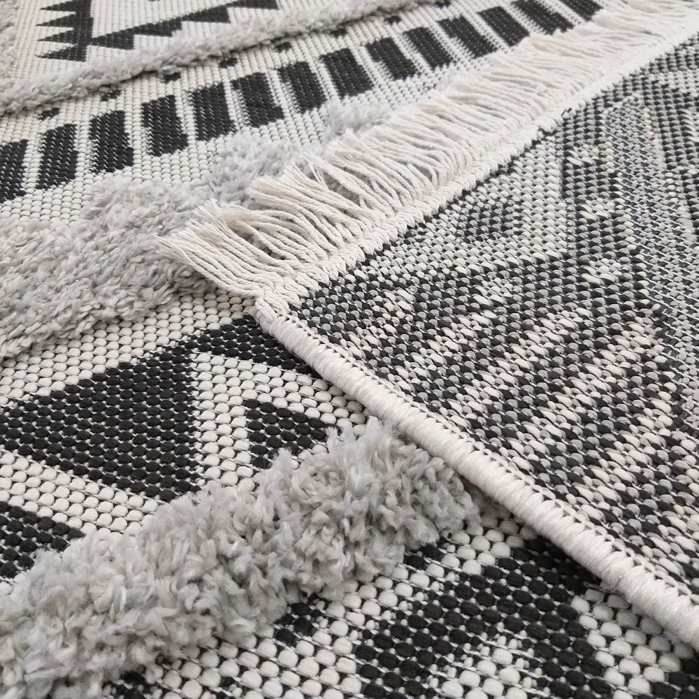 Tapis noir et blanc à motifs géométriques avec des sections touffues gris clair et des franges blanches