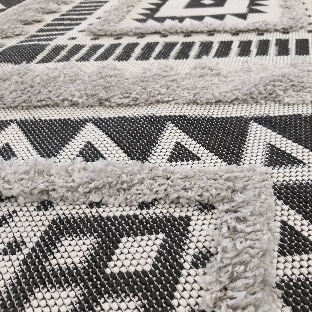 Tapis texturé en noir, blanc et gris clair, avec des motifs géométriques et des bandes moelleuses en relief