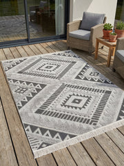 Tapis rectangulaire texturé gris clair et foncé à motifs géométriques ethniques, frangé, dans un espace de vie