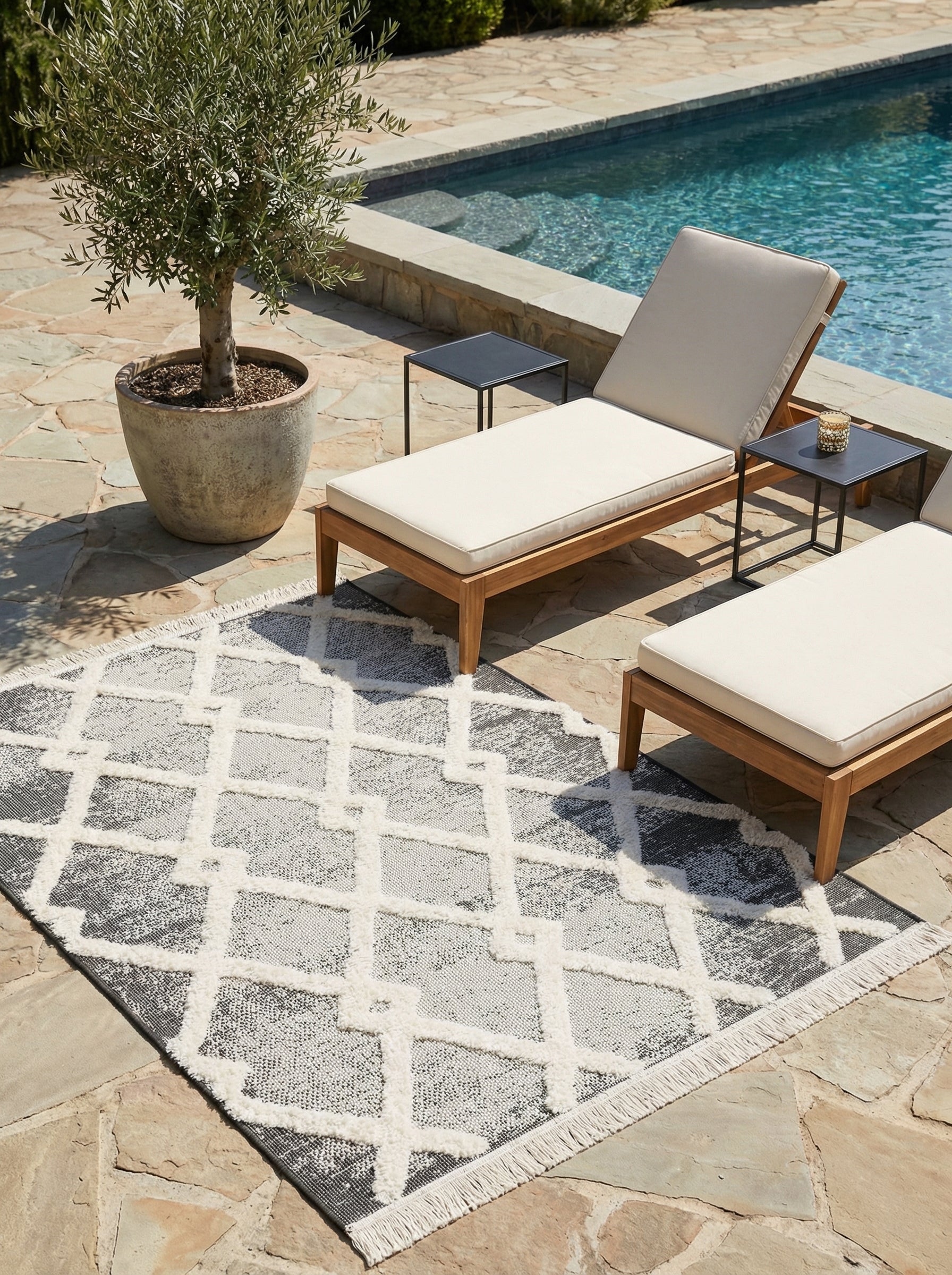 Tapis rectangulaire à motifs géométriques blanc cassé duveteux sur fond gris foncé et clair, avec franges, sur une terrasse près d'une piscine