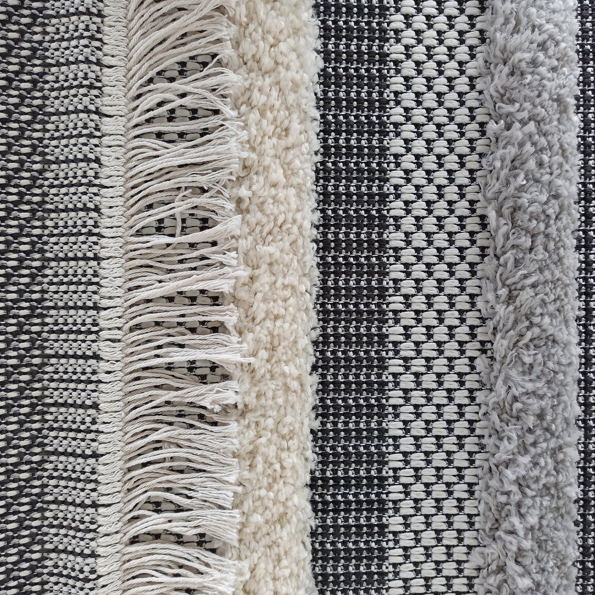 Tapis à motifs rayés verticaux mêlant textures tissées en damier noir et blanc, franges claires, et bandes bouclées beige et gris