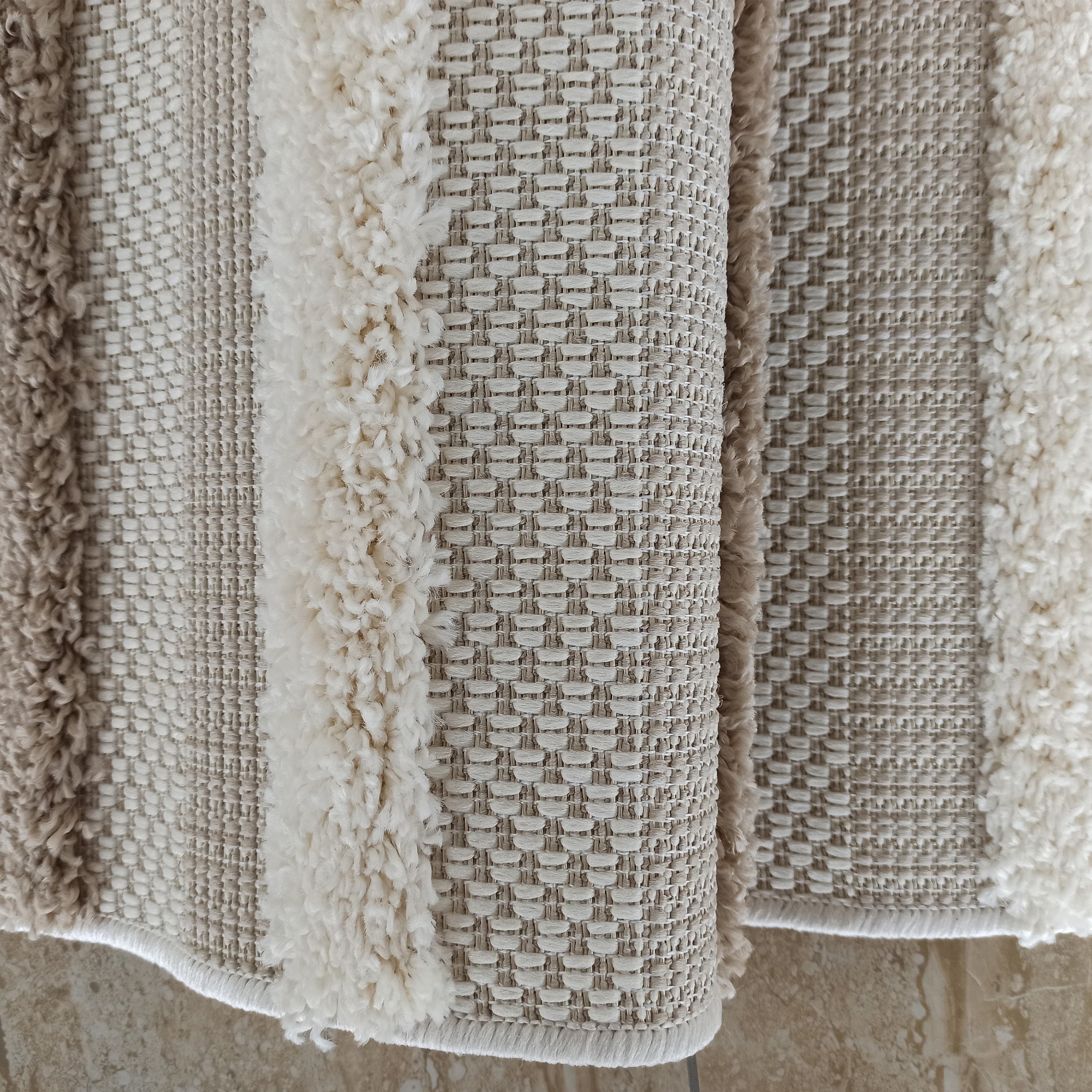 Tapis aux nuances de beige et crème, présentant des bandes de tissu bouclé et des zones au tissage régulier