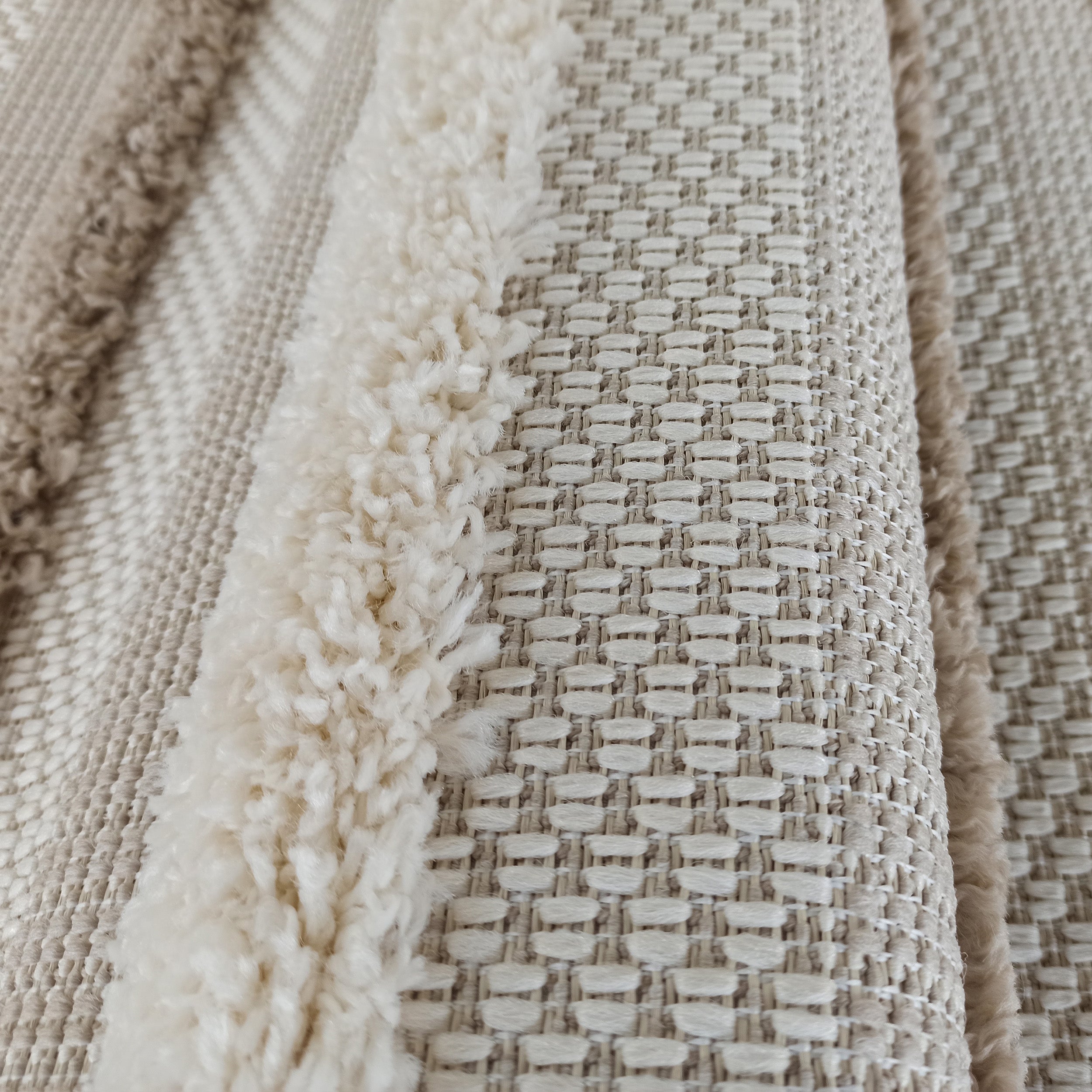 Tapis texturé beige clair et crème, présentant des bandes de longs poils doux alternant avec des motifs tissés en relief