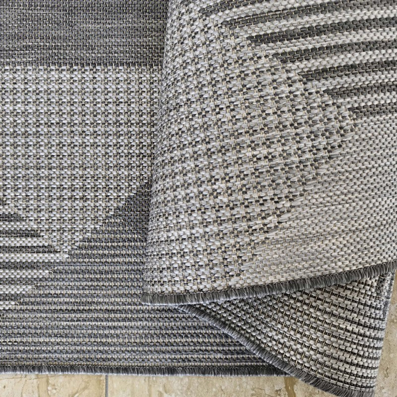 Tapis tissé gris et blanc cassé avec des motifs géométriques et des rayures, partiellement plié