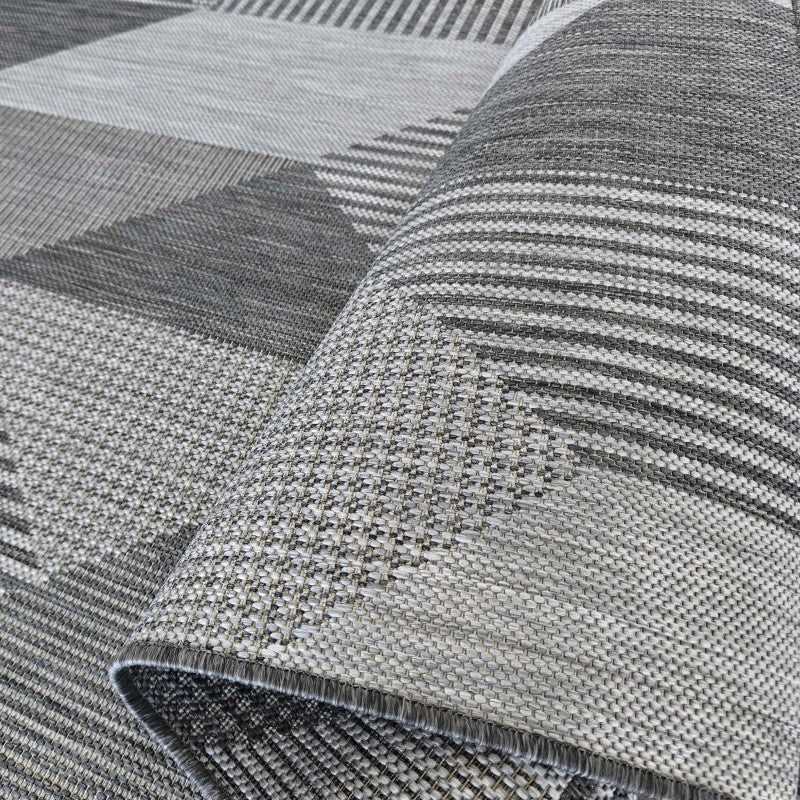 Tapis tissé gris aux motifs géométriques variés comme des rayures et des triangles, partiellement enroulé