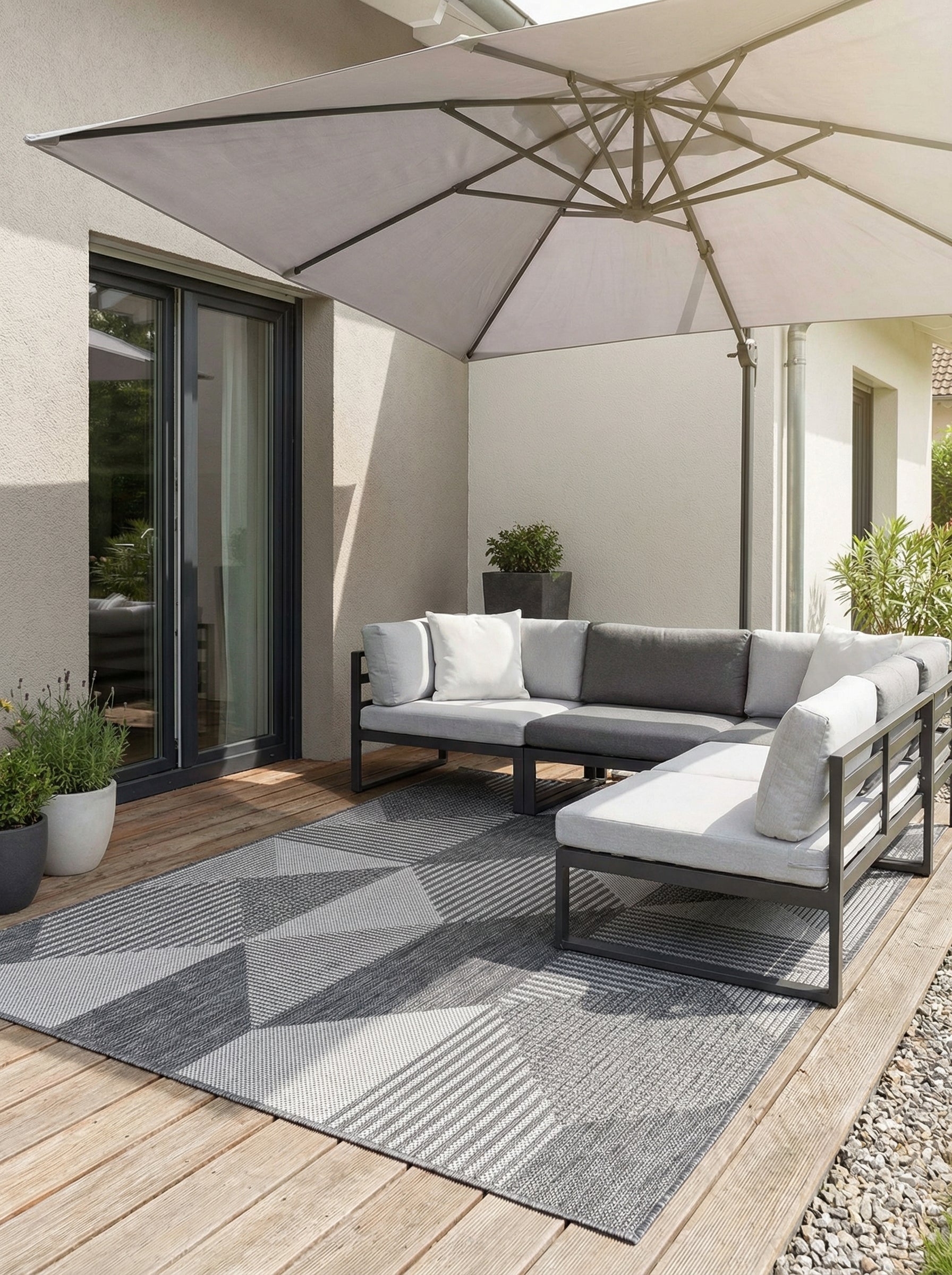 Tapis rectangulaire gris clair et foncé aux motifs géométriques variés sur une terrasse en bois avec salon de jardin