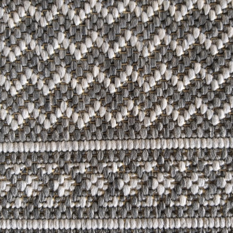 Gros plan sur un tapis texturé avec des motifs géométriques en chevrons gris clair et gris foncé, et des rayures horizontales claires