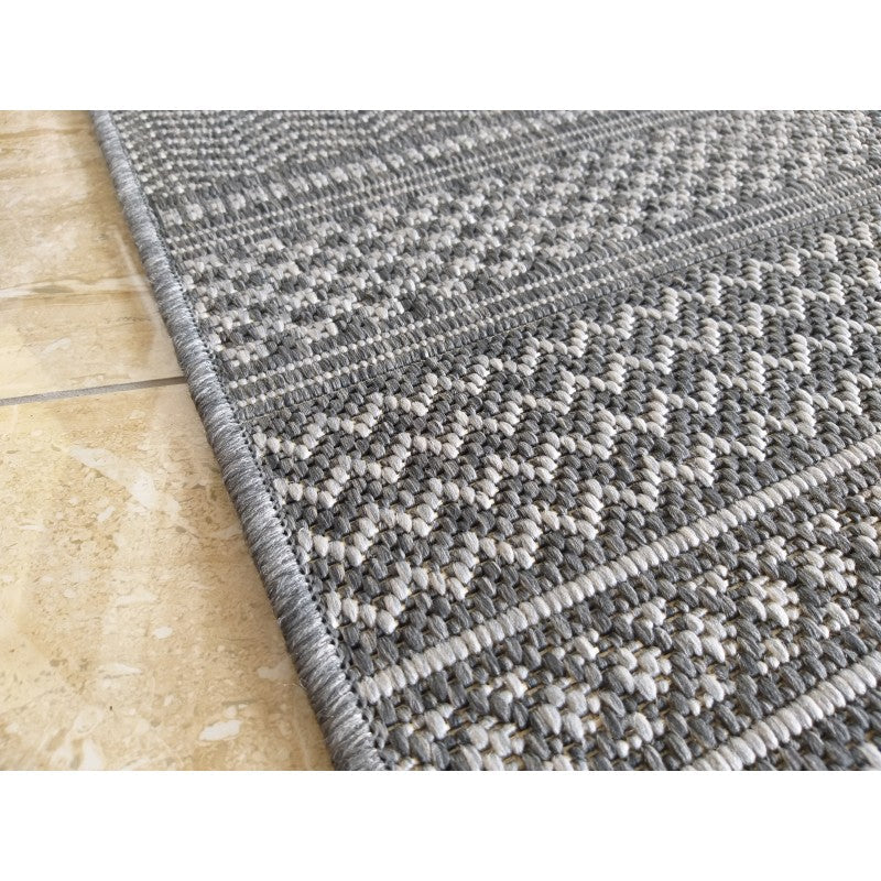 Tapis en textile tissé gris et blanc présentant des motifs géométriques à chevrons et lignes