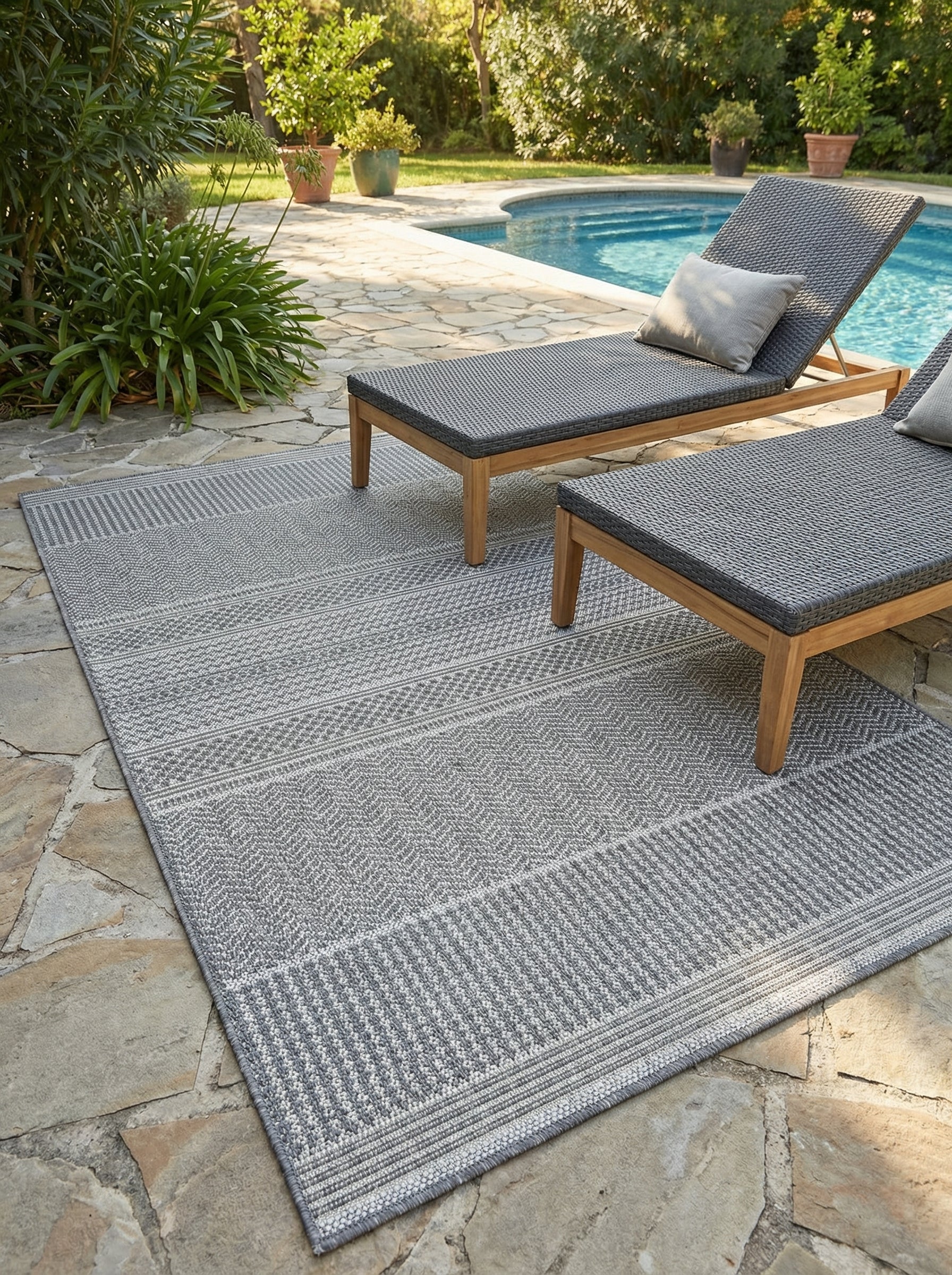 Tapis rectangulaire gris clair et foncé à motifs géométriques tissés, posé sur une terrasse en pierre près d'une piscine