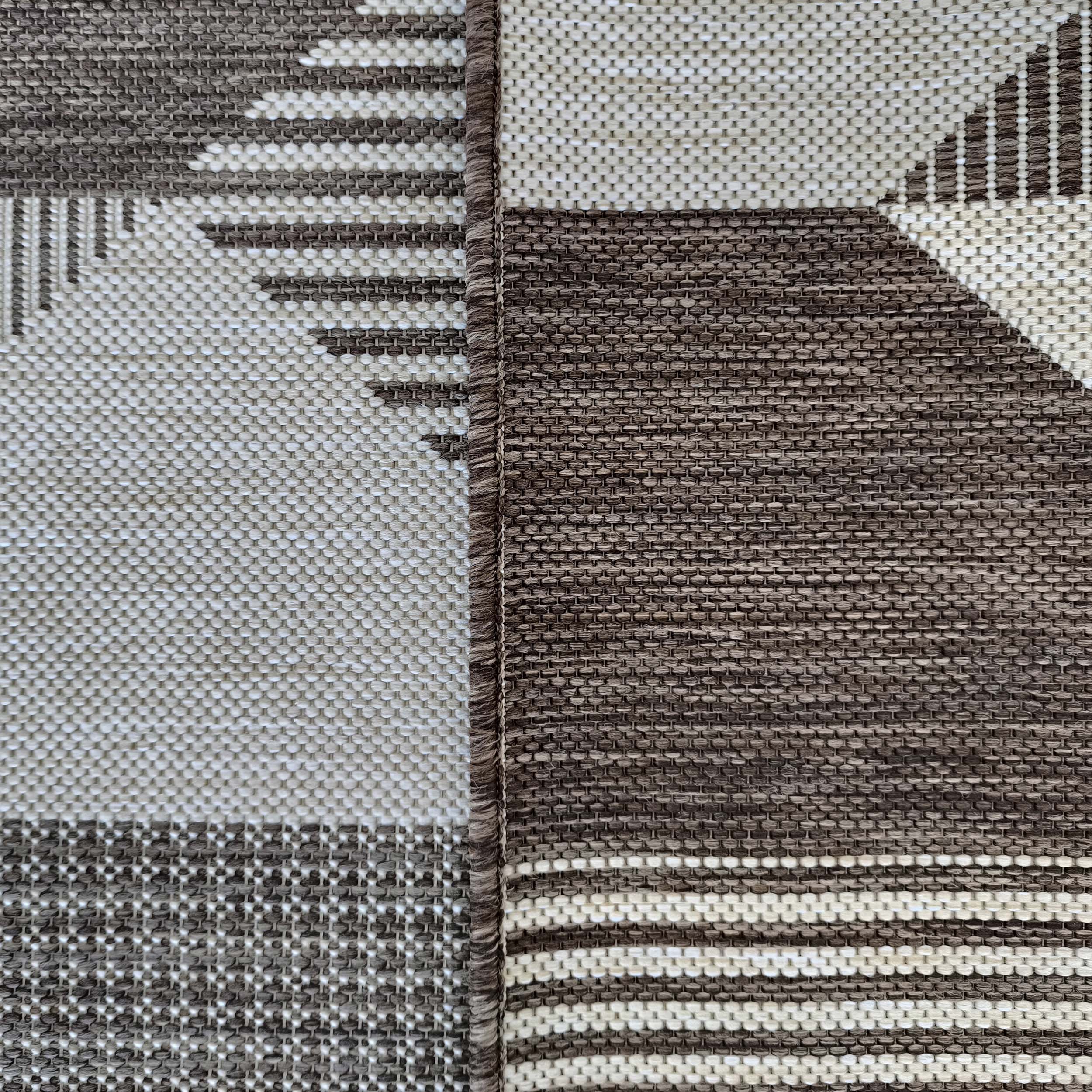 Tapis tissé présentant des motifs géométriques complexes en nuances de marron, beige et blanc cassé, avec une couture centrale apparente