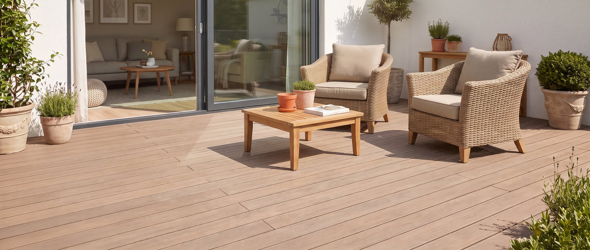 Une terrasse en bois clair est aménagée de fauteuils tressés et de plantes en pot, sans tapis