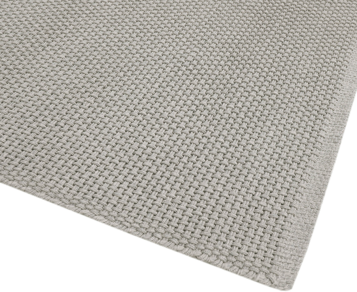 Le maillage serré et texturé du tapis gris clair met en valeur sa matière