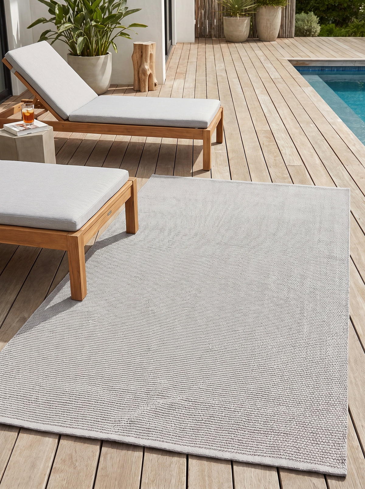 Avec son tissage texturé en gris clair, le tapis d'extérieur structure l'espace sur la terrasse en bois près de la piscine