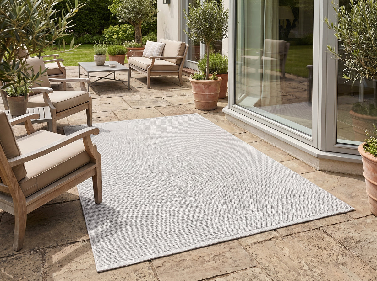 Le tissage fin et texturé de ce tapis rectangulaire gris clair d'extérieur délimite un espace sur la terrasse