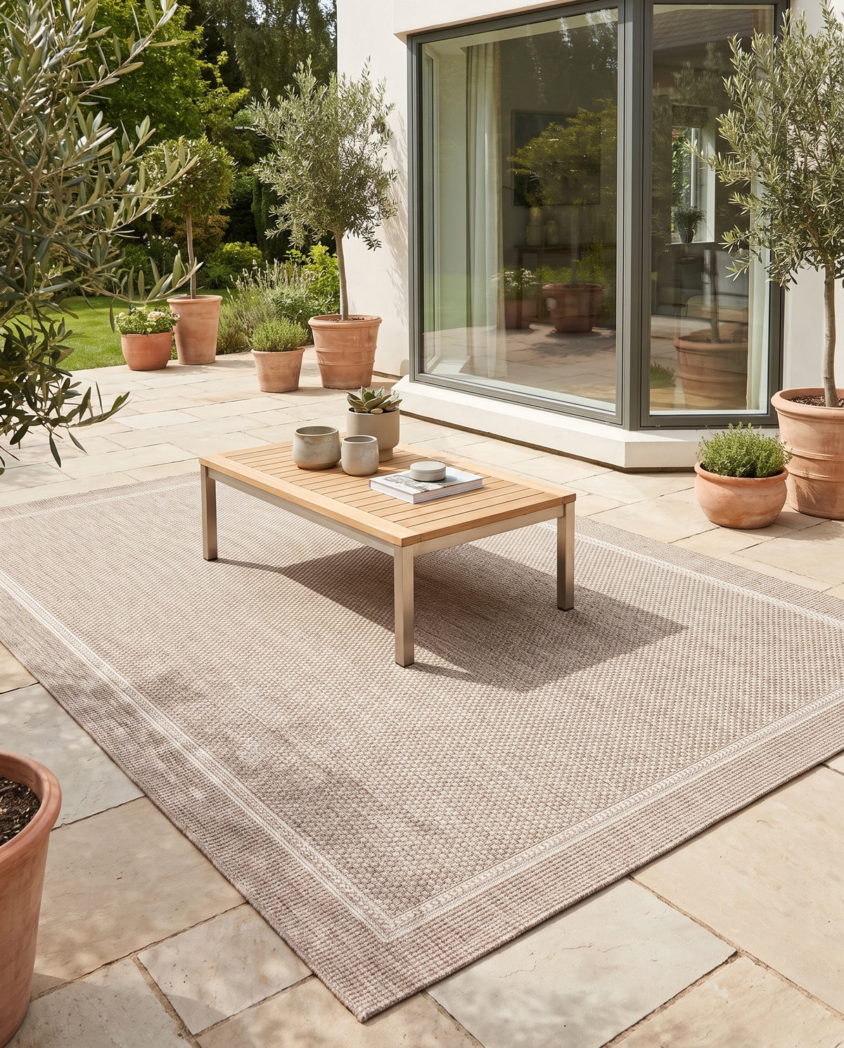 Des tons gris et ivoire aux motifs tissés et à la bordure marquée pour ce tapis d'extérieur sur une terrasse