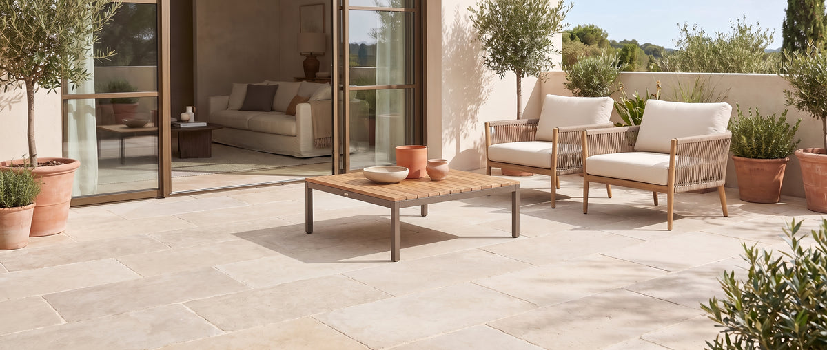 Une terrasse méditerranéenne sans tapis, avec son sol de dalles claires, des fauteuils et des oliviers en terre cuite