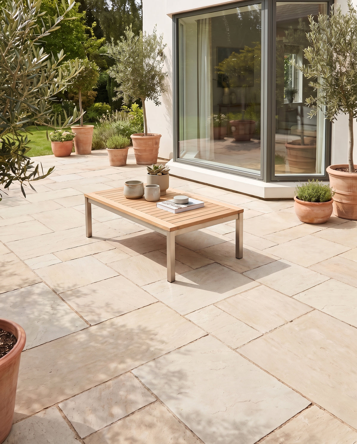 Sol nu de dalles claires, cette terrasse présente une table basse en bois et plusieurs oliviers en pots