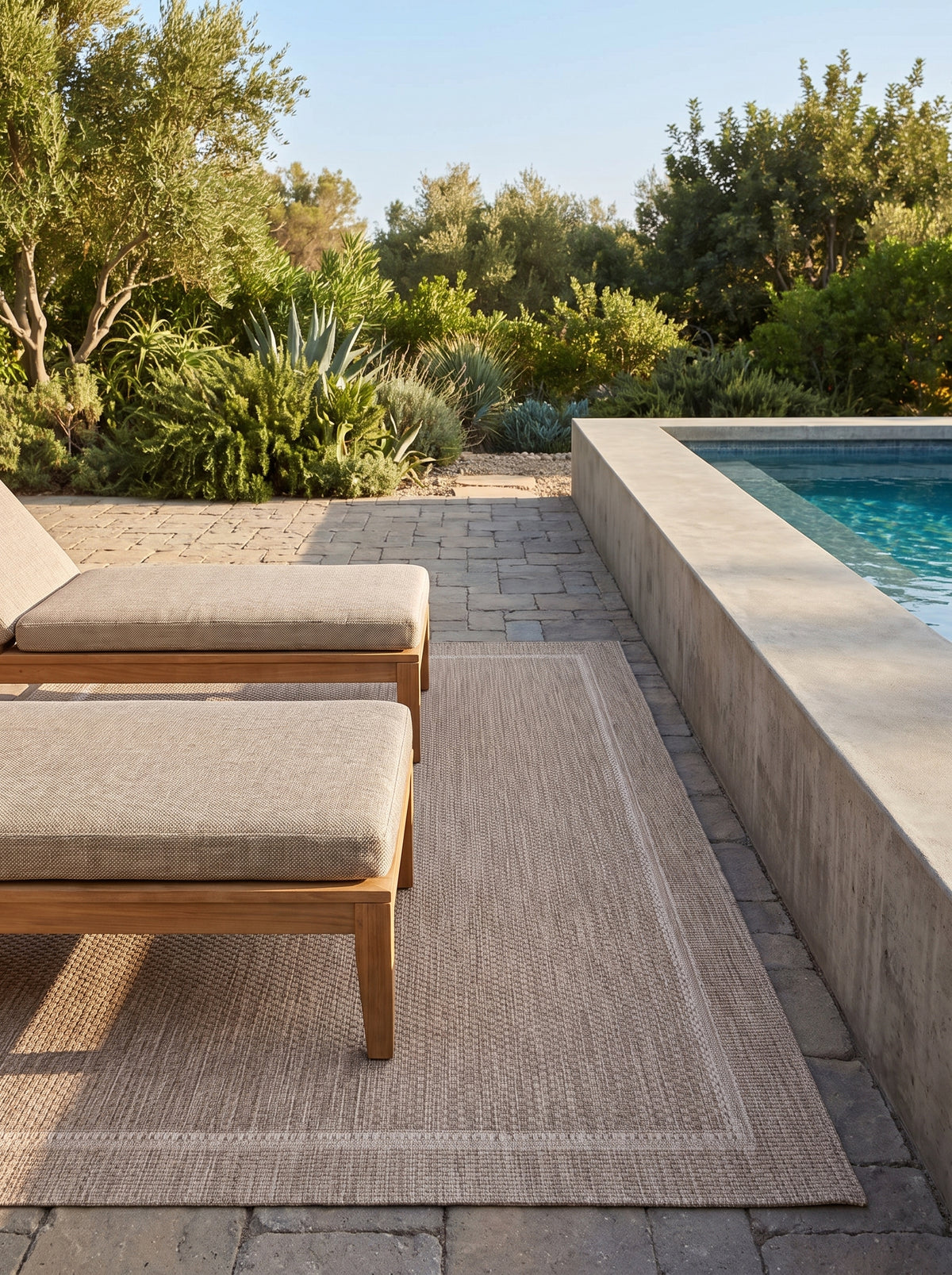 Un revêtement rectangulaire gris et ivoire, à la texture finement tissée et bordure subtile, habille une terrasse de piscine