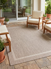 La bordure finement dessinée d'un tapis d'extérieur gris et ivoire, sur une terrasse ensoleillée