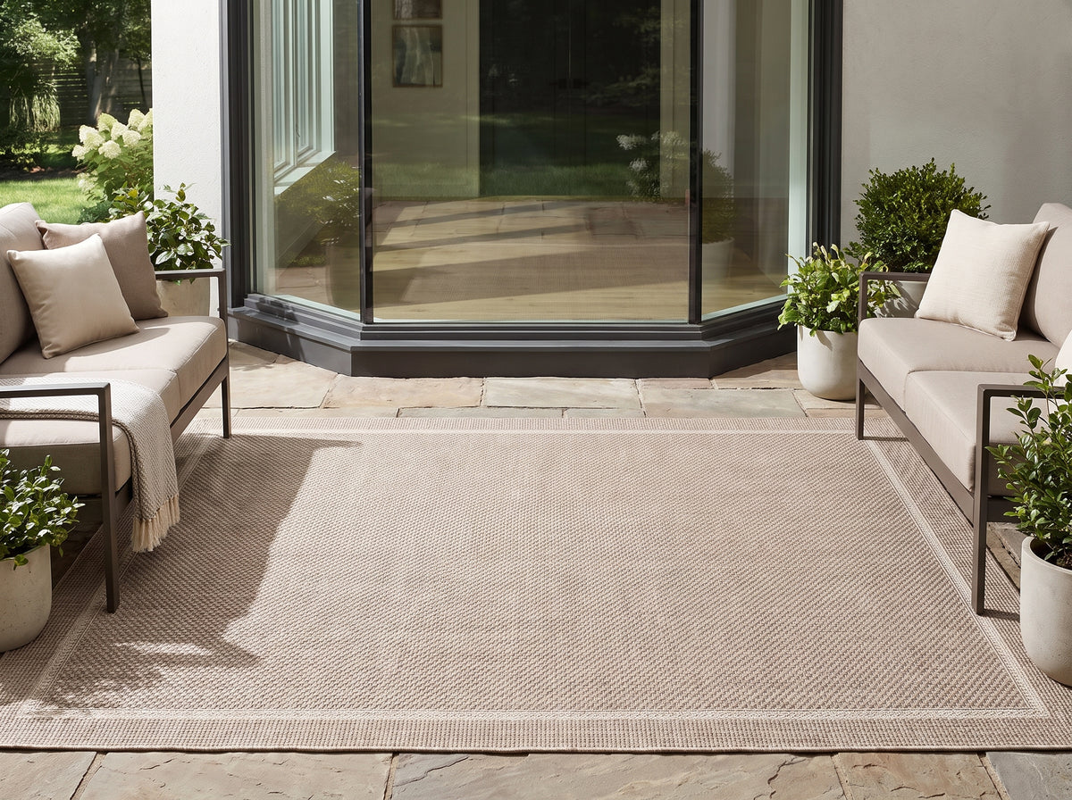 Sur une terrasse, un tapis d'extérieur gris et ivoire présente un tissage serré et une bordure contrastée