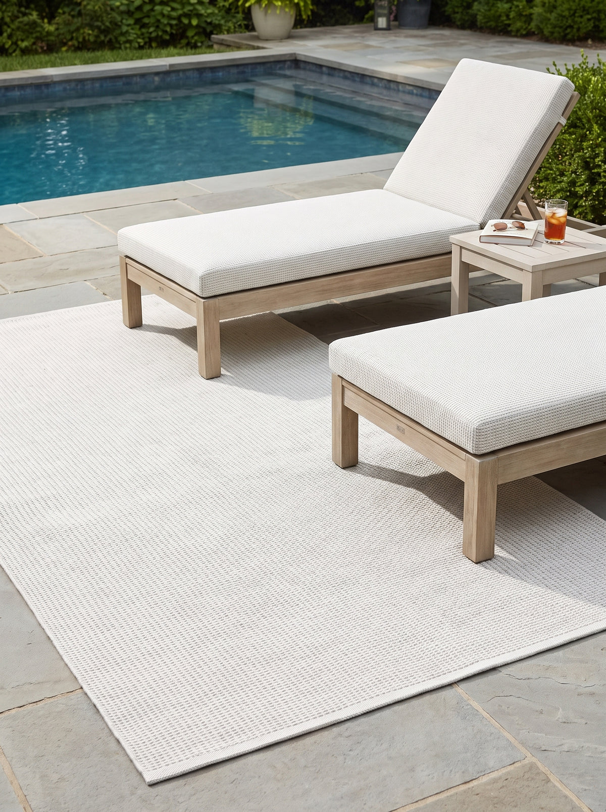 Ein elfenbeinfarbener Outdoor-Teppich mit regelmäßig texturierter Webart liegt auf einer Steinterrasse am Pool