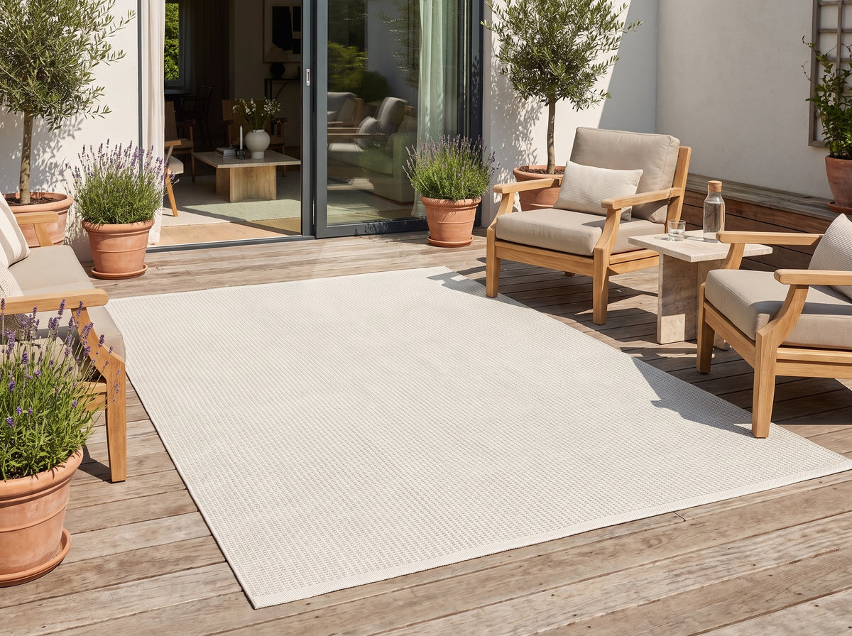 Sur une terrasse en bois, un tapis d'extérieur ivoire rectangulaire affiche un fin tissage régulier
