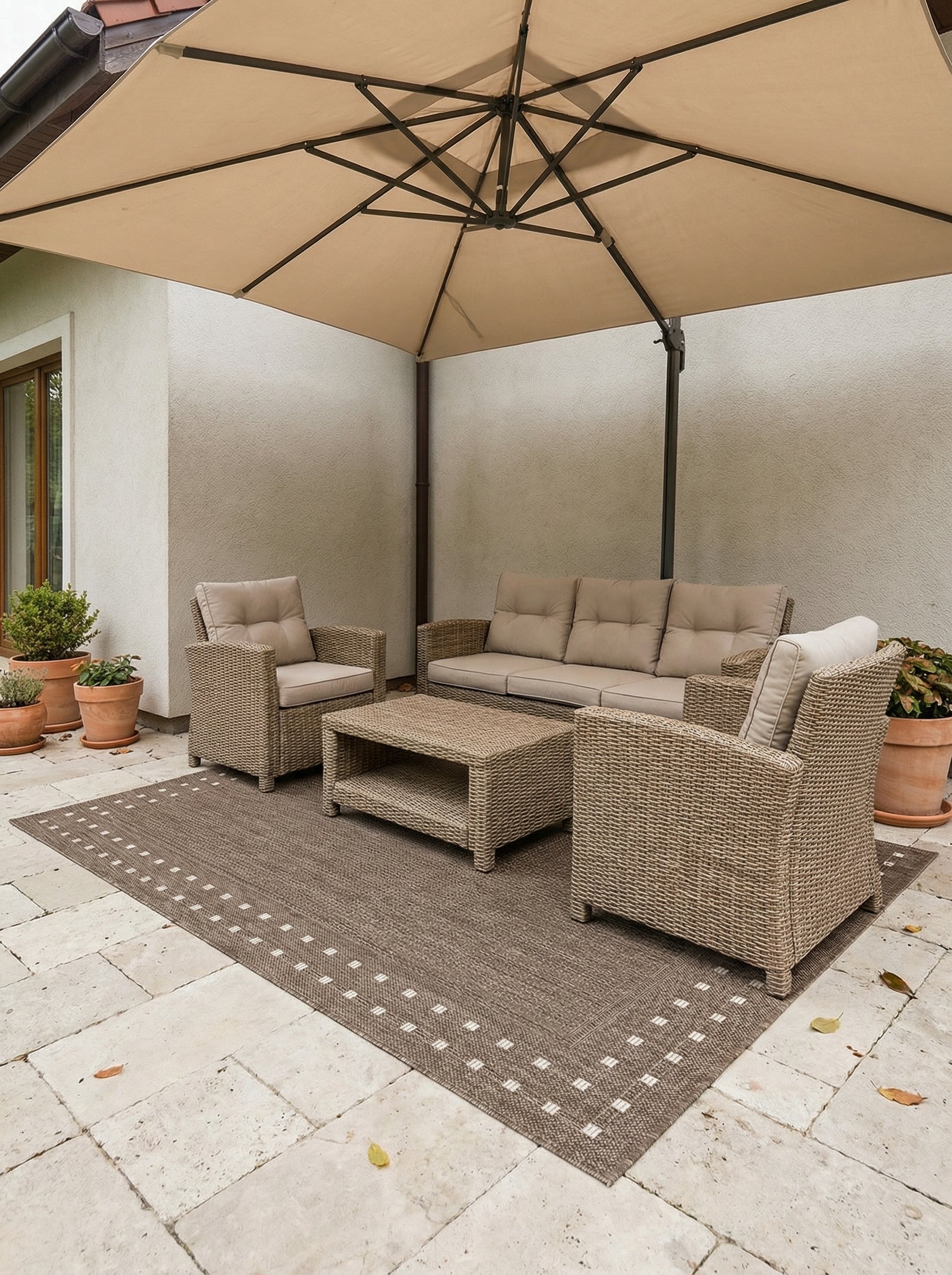 Tapis rectangulaire tissé gris-brun avec un motif de bordure à petits carrés blancs, sur une terrasse aménagée