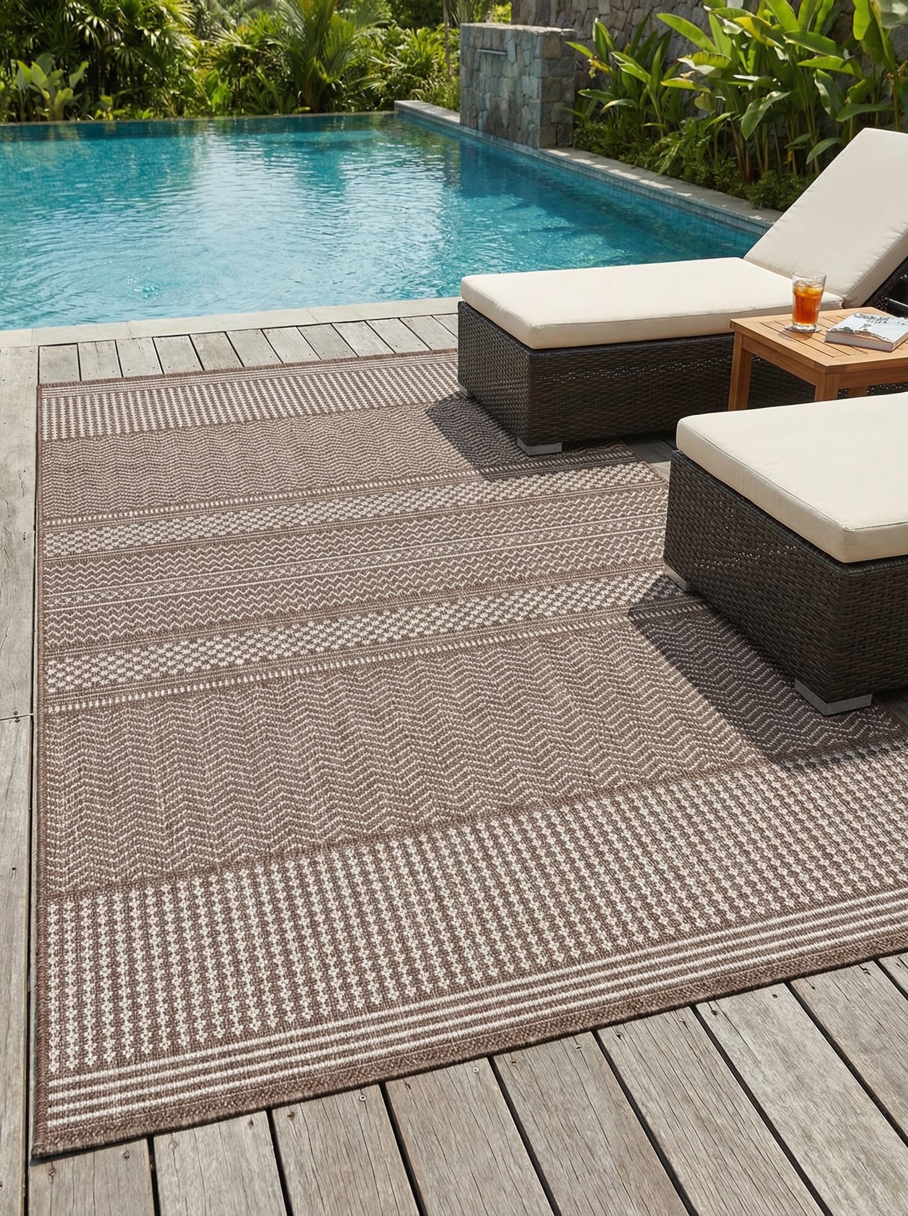Tapis rectangulaire tressé marron et beige clair, à motifs géométriques en bandes de chevrons et rayures, sur une terrasse en bois près d'une piscine