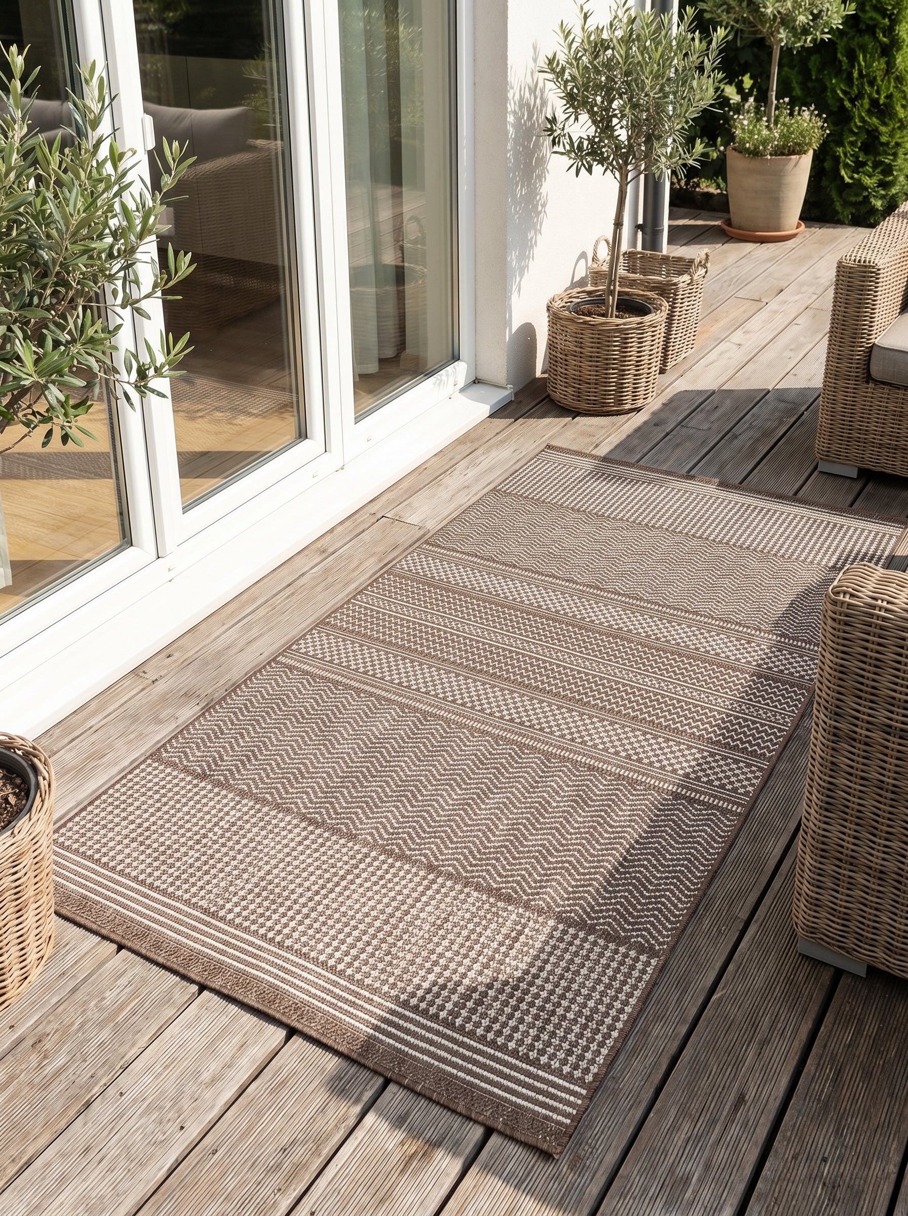 Tapis rectangulaire brun et écru aux motifs géométriques variés (chevrons, carrés), sur une terrasse en bois