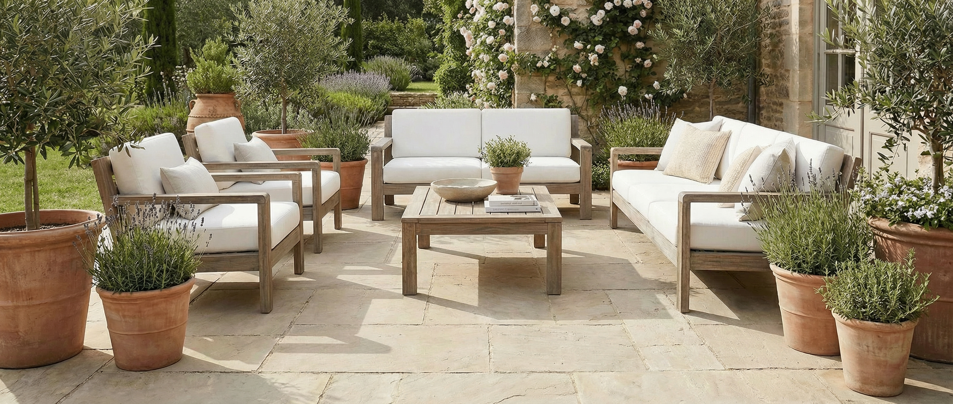 Terrasse en pierre, mobilier en bois clair, coussins blancs. Espace vide, potentiel déco pour un tapis rectangulaire
