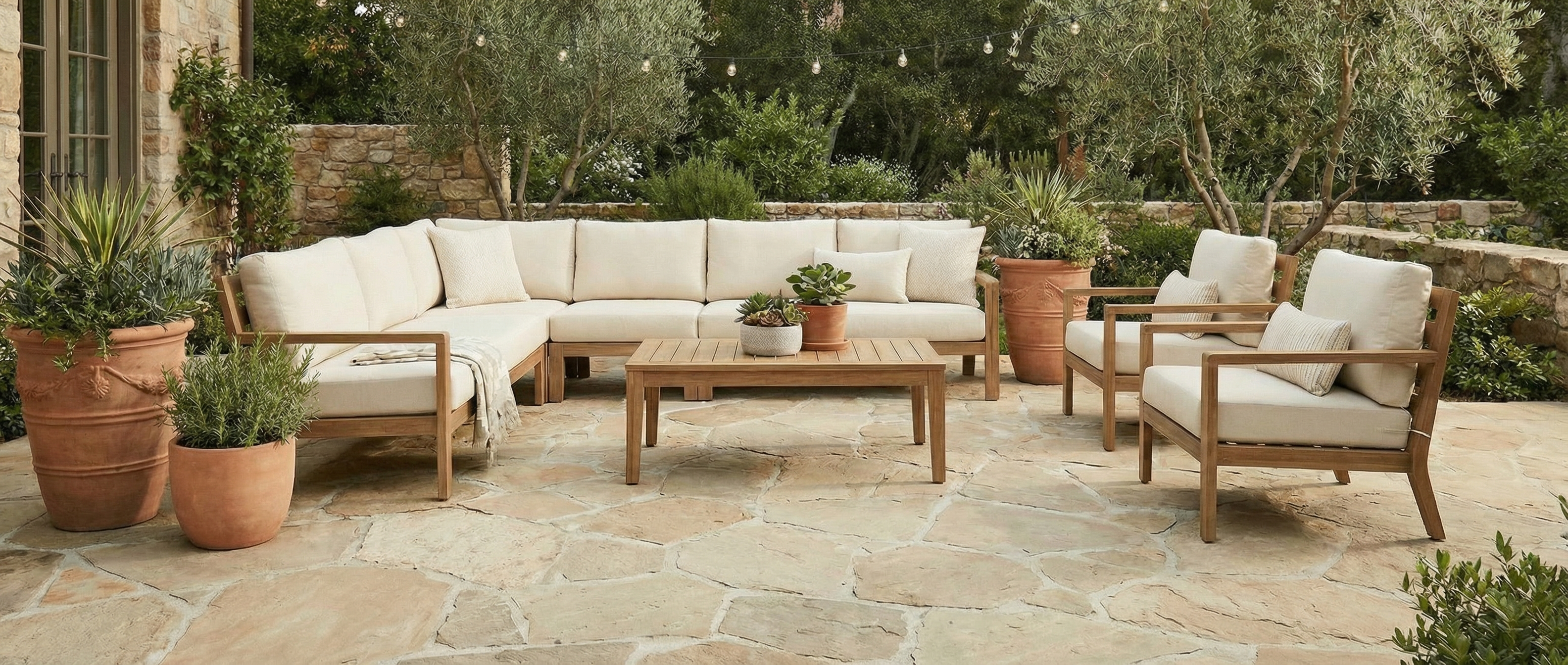 Patio avec mobilier en bois clair et coussins beiges. Sol en pierre beige. Espace vide, potentiel déco