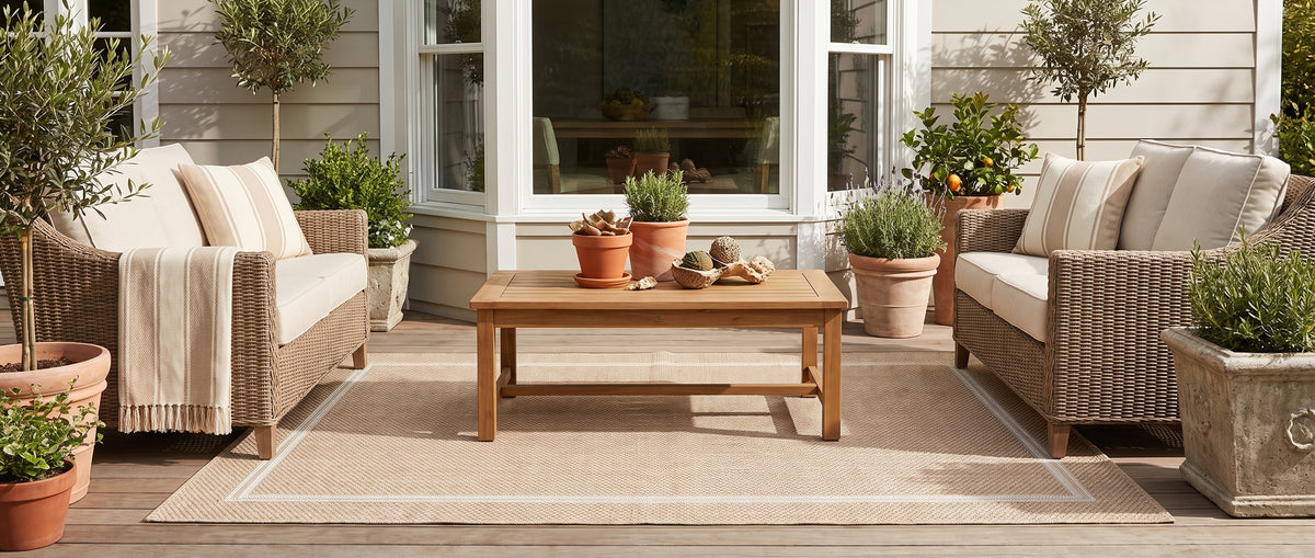 Sur une terrasse en bois, un tapis extérieur sable au tissage bouclé, orné d'un cadre rectangulaire ivoire