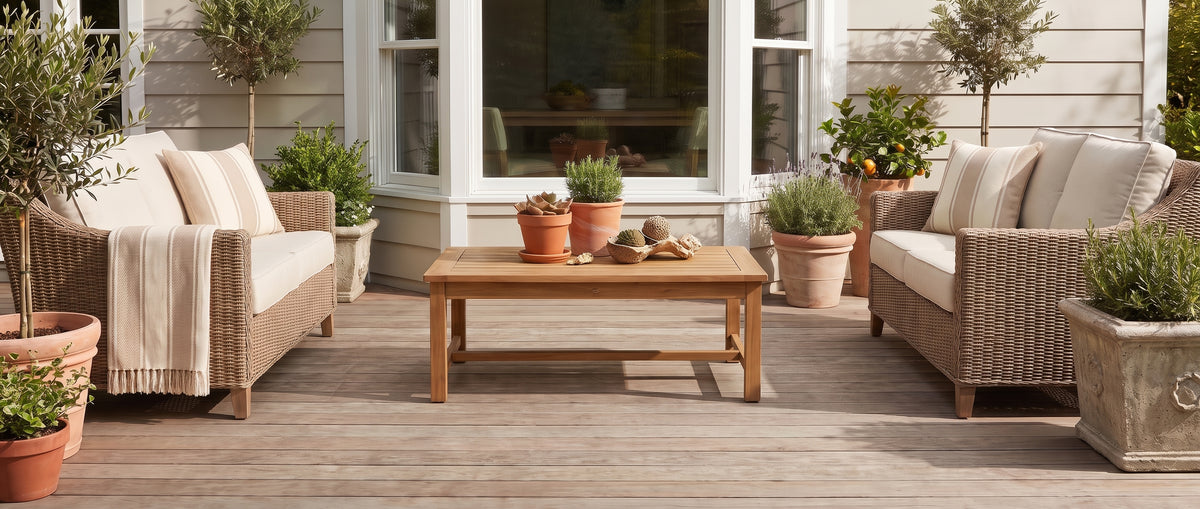 Un salon extérieur sur une terrasse en bois nu, avec deux fauteuils en osier, une table basse et des plantes en pots
