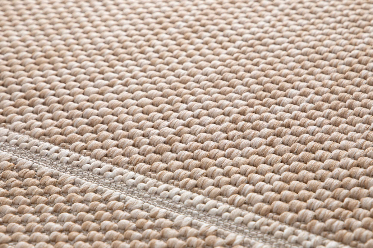 Tissage bouclé d'un tapis extérieur sable et ivoire, détaillant les reliefs de la matière et une fine bande tissée à plat