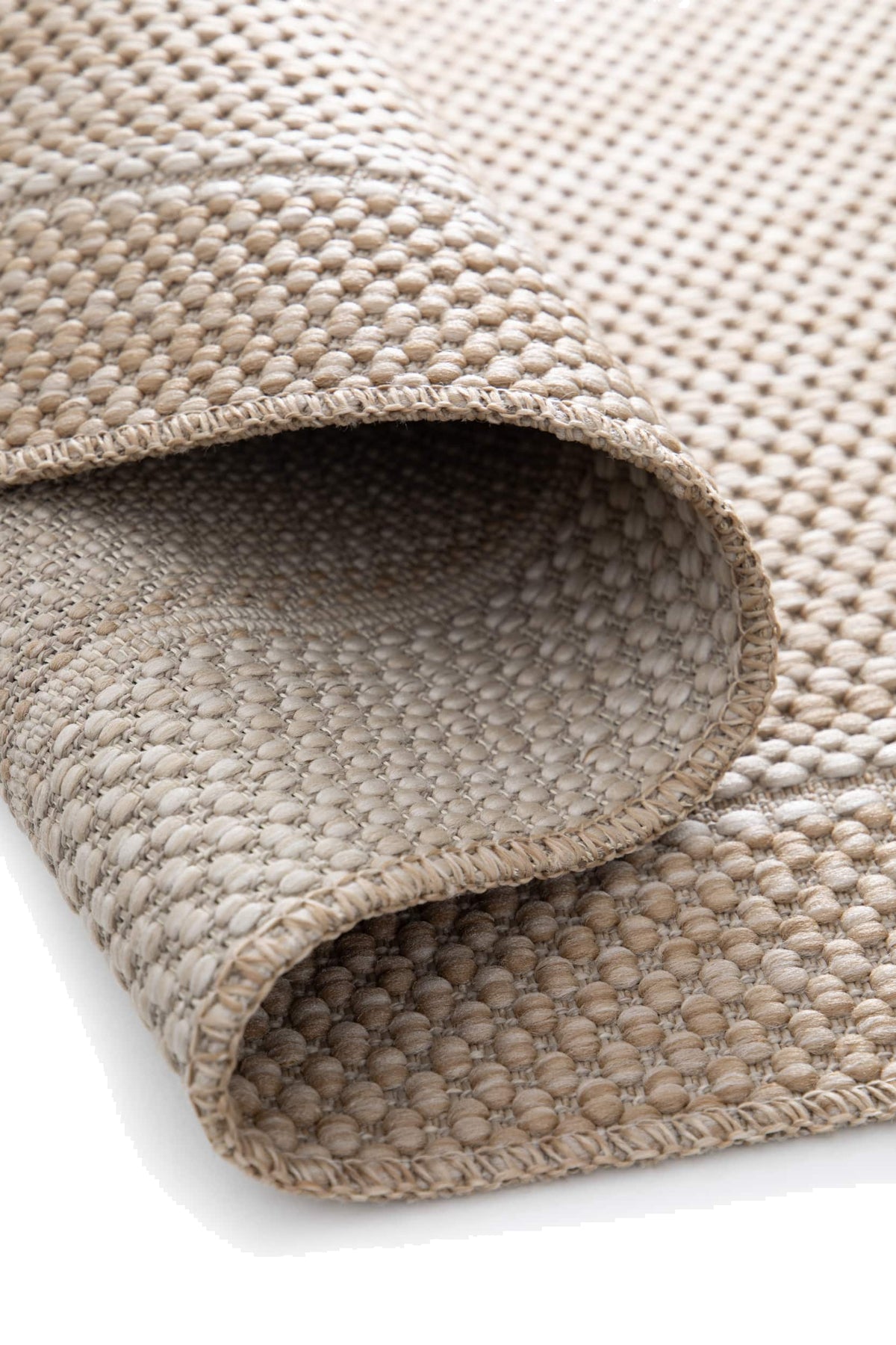 Le relief du tissage bouclé sable et ivoire d'un tapis extérieur roulé, avec son envers contrasté