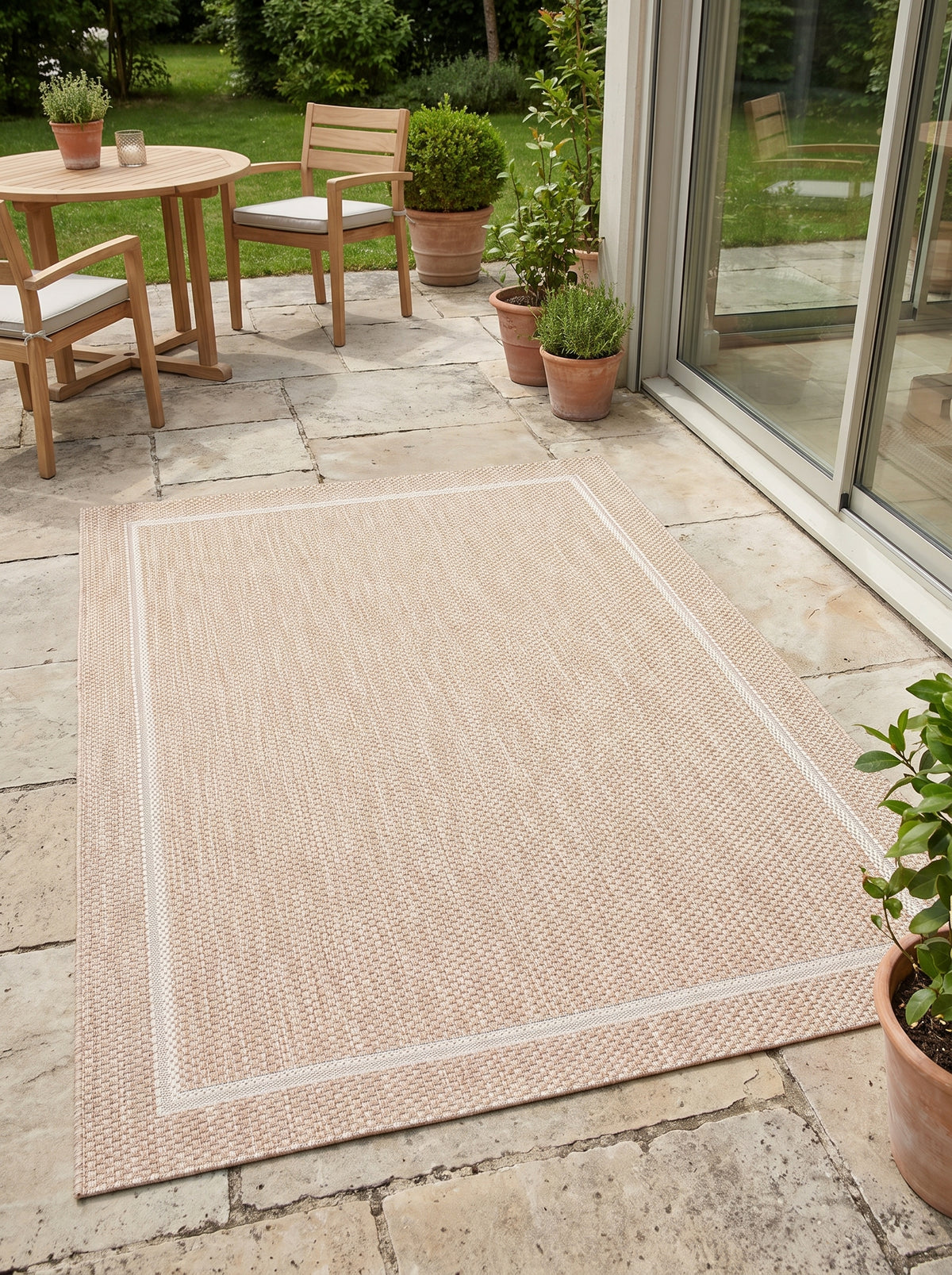 Ivory frame outlines a rectangular sand outdoor rug with looped weave on a paved terrace