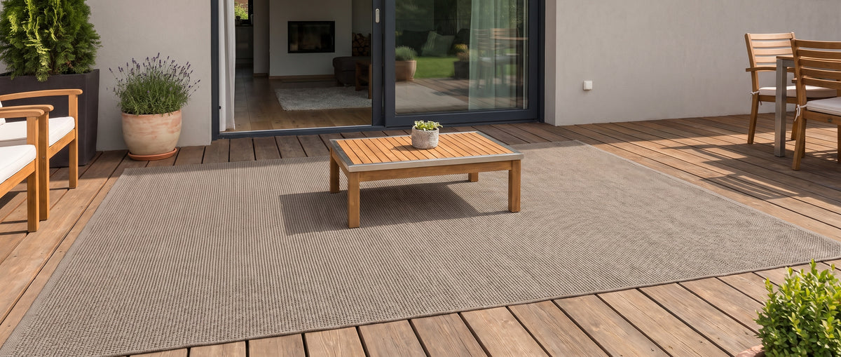 Le grain discret d'un tapis rectangulaire taupe chaud habille cette terrasse en bois