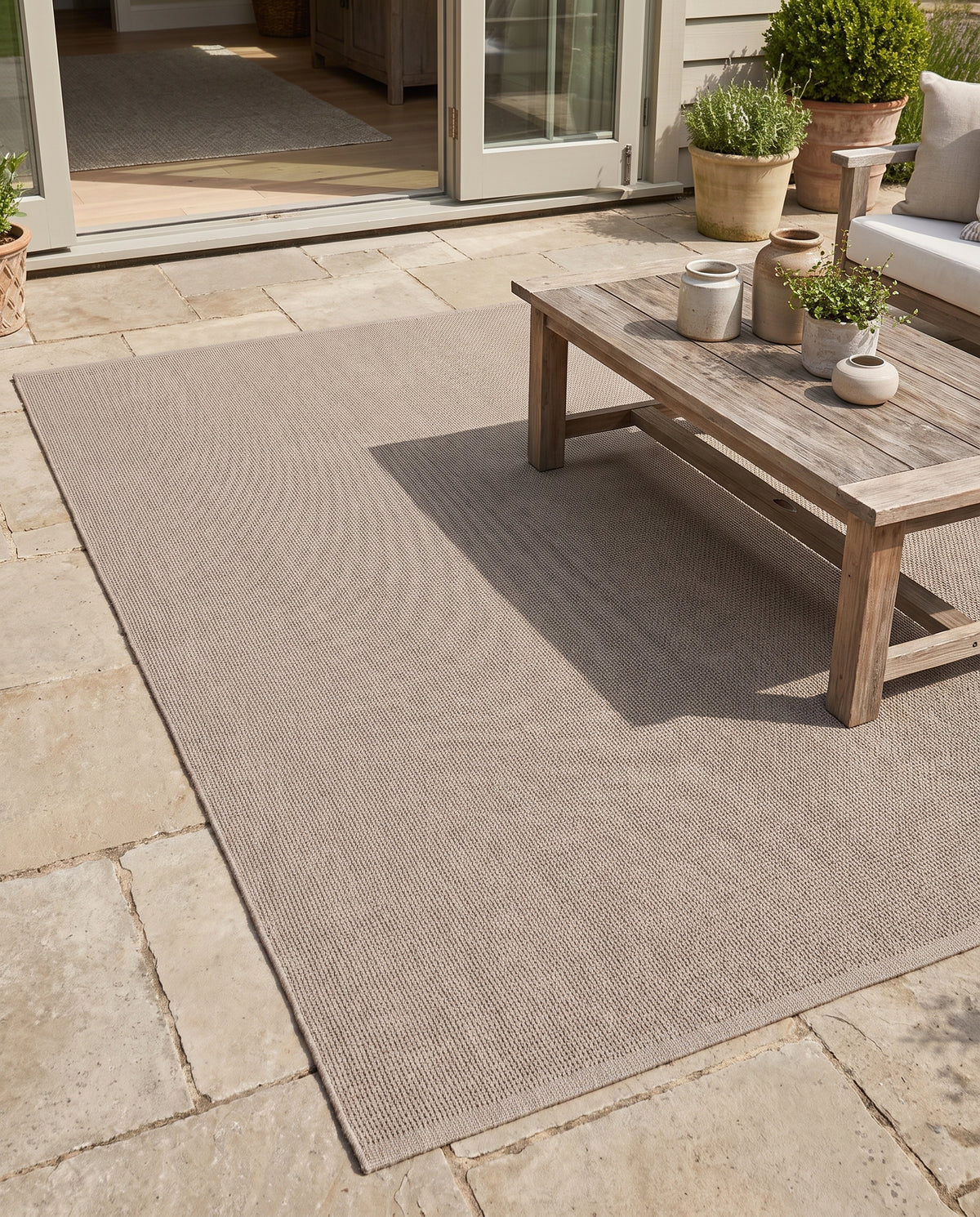Son tissage fin et sa teinte taupe chaude animent ce tapis d'extérieur rectangulaire sur une terrasse en dalles