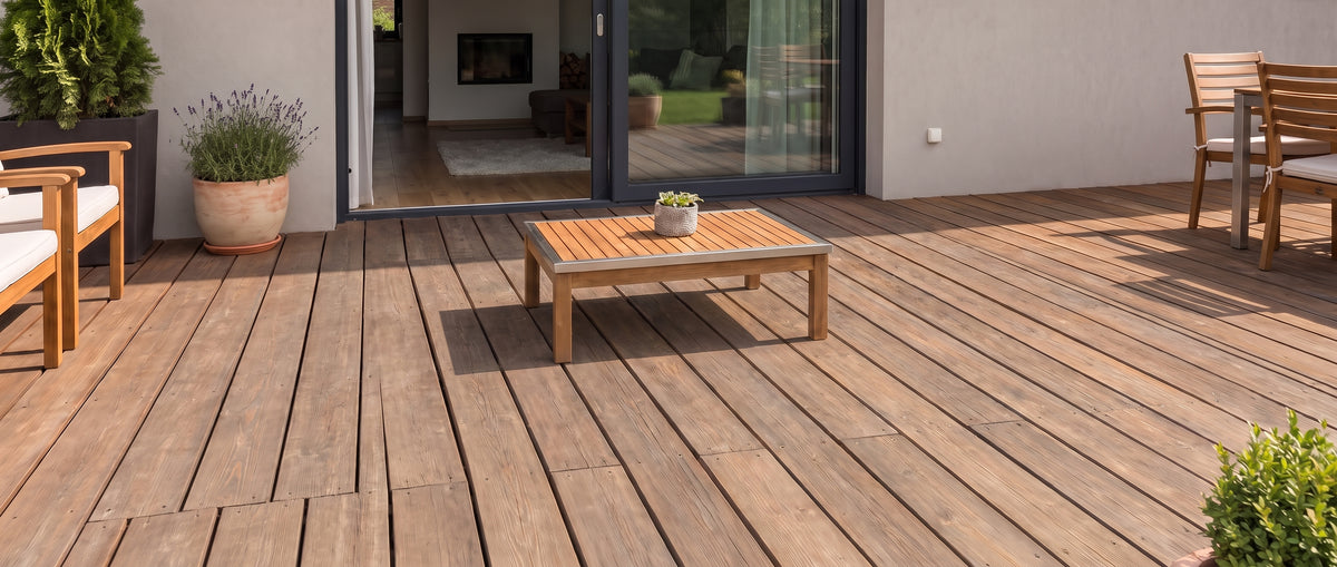 Sur le sol nu de la terrasse en bois, un salon de jardin et des pots de plantes ornent l'espace