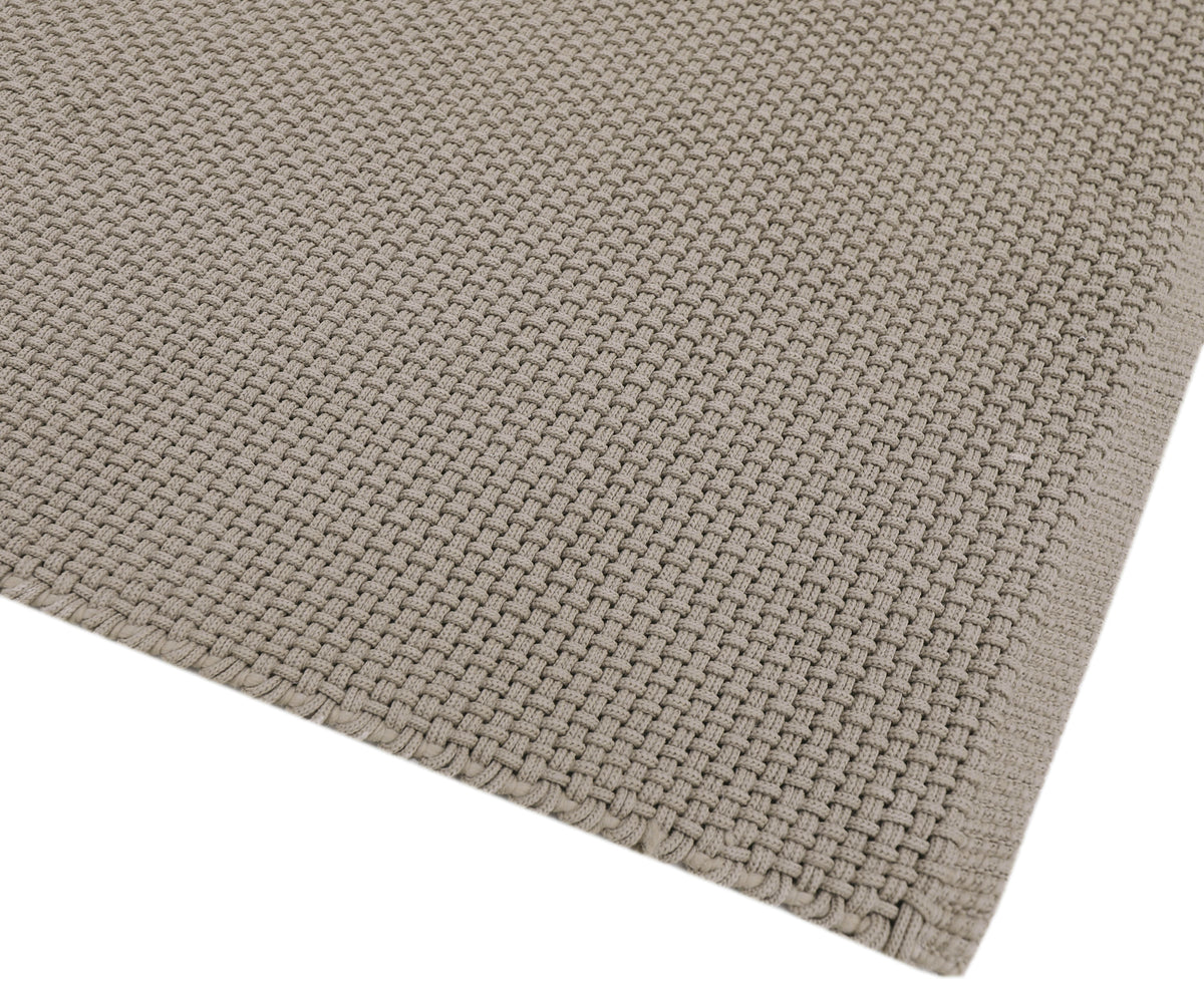 La surface texturée du tapis taupe d'extérieur révèle un tissage serré et le soin de sa bordure