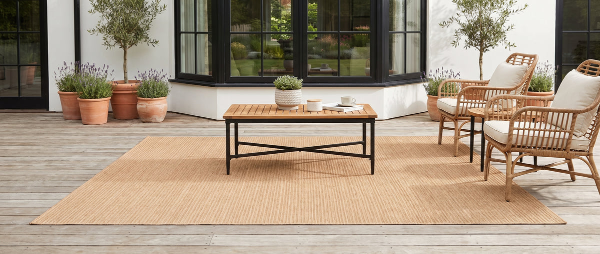 Un tapis d'extérieur rectangulaire terracotta clair, au tissage côtelé, s'intègre à un salon de terrasse ensoleillé