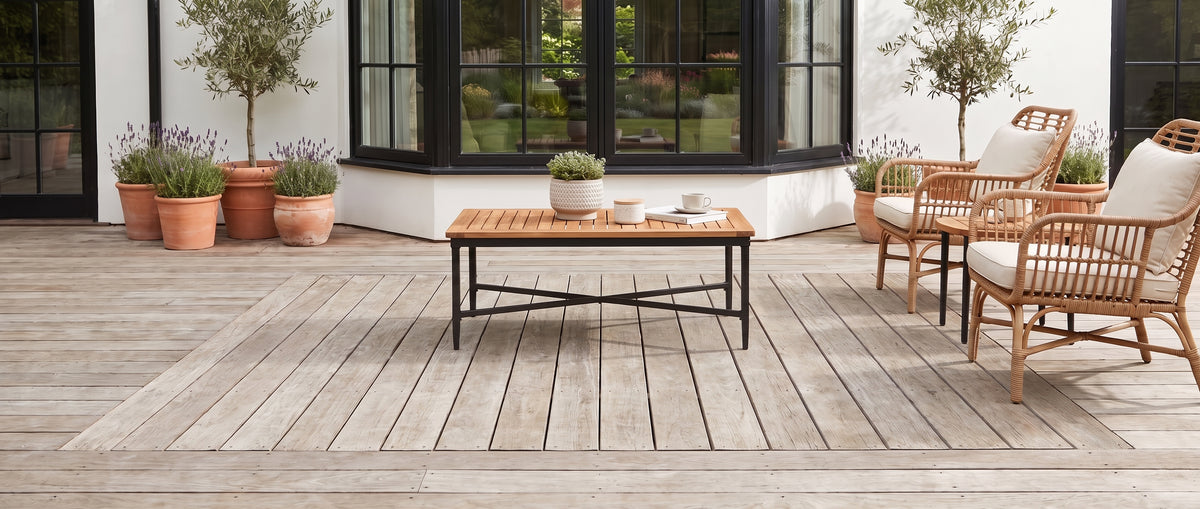 Un salon de terrasse sobre est aménagé sur un sol en bois nu, avec fauteuils en rotin et table basse