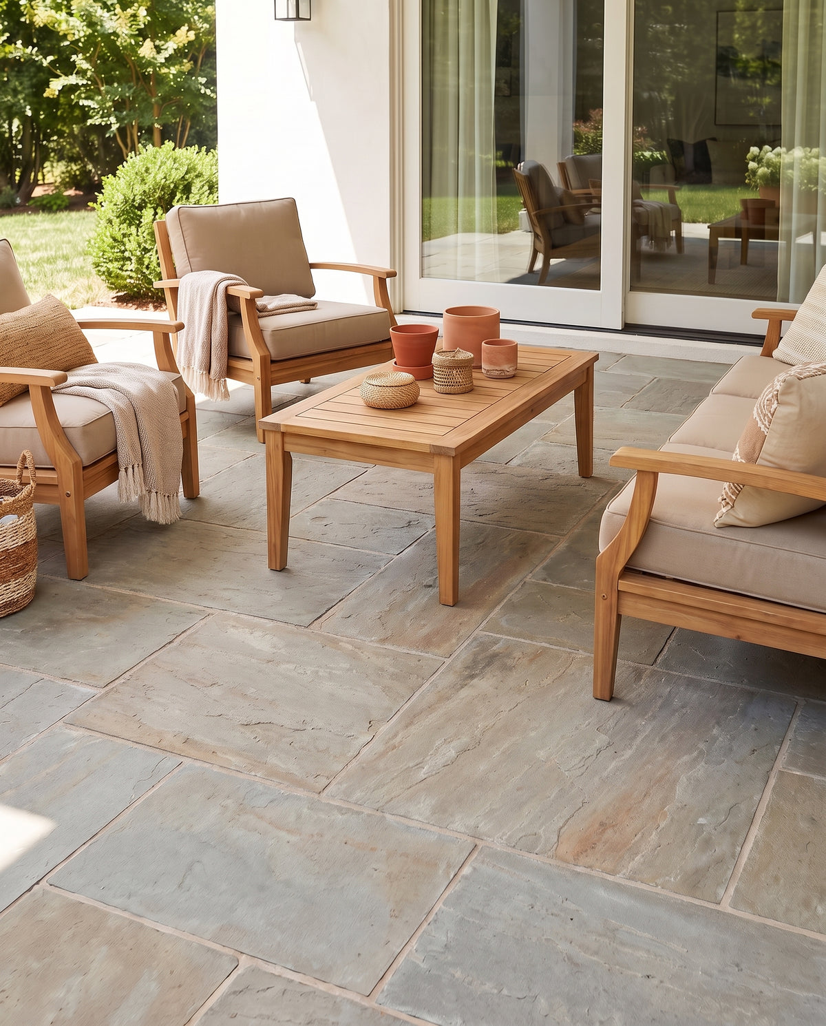 Une terrasse sans tapis, au sol de dalles nues, meublée d'un salon en bois clair et de pots terracotta