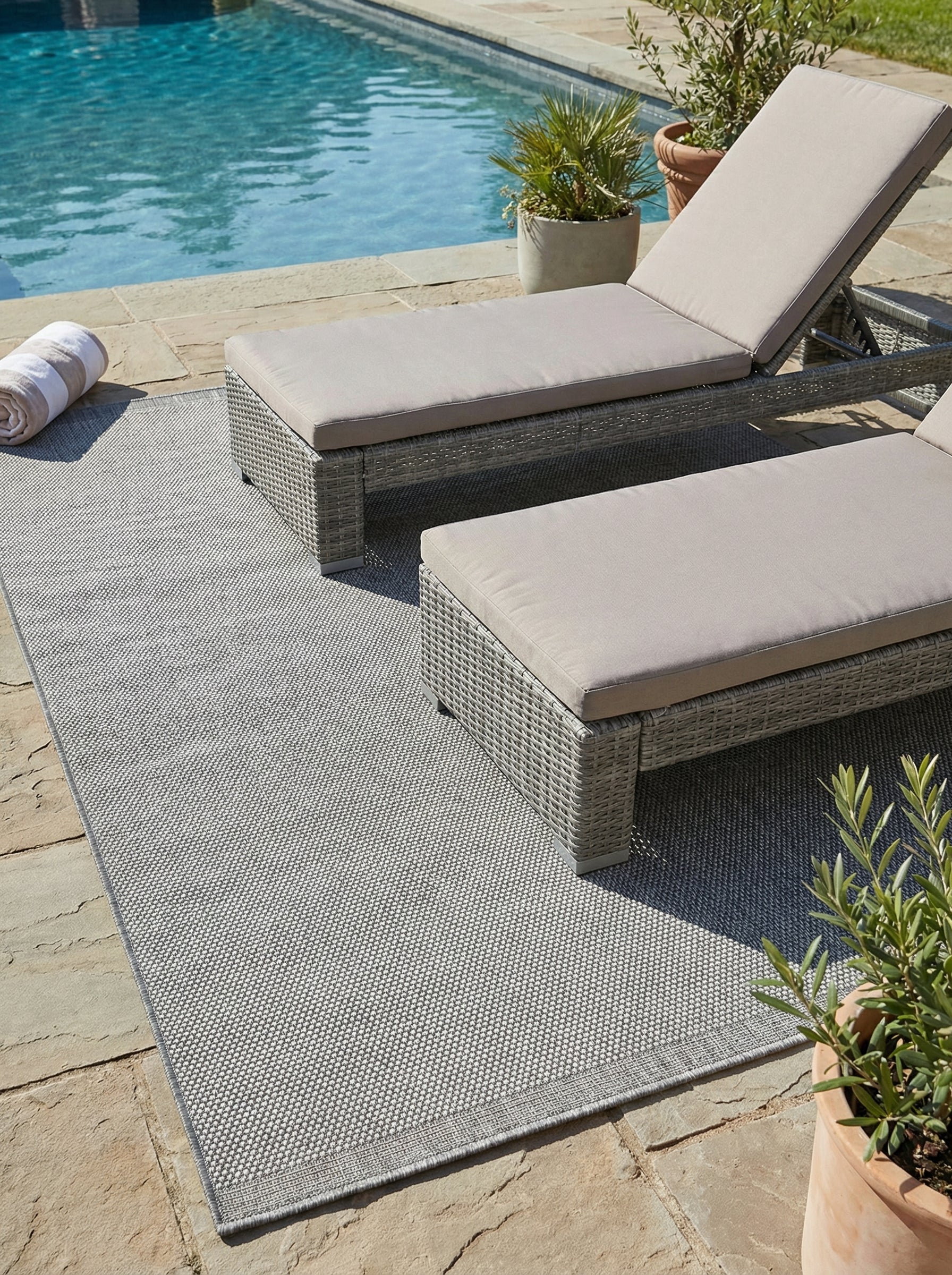 Tapis rectangulaire gris chiné texturé posé sur une terrasse en dalles de pierre avec des transats près d'une piscine