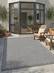 Tapis rectangulaire gris tissé effet poivre et sel, avec une bordure gris foncé unie, sur une terrasse
