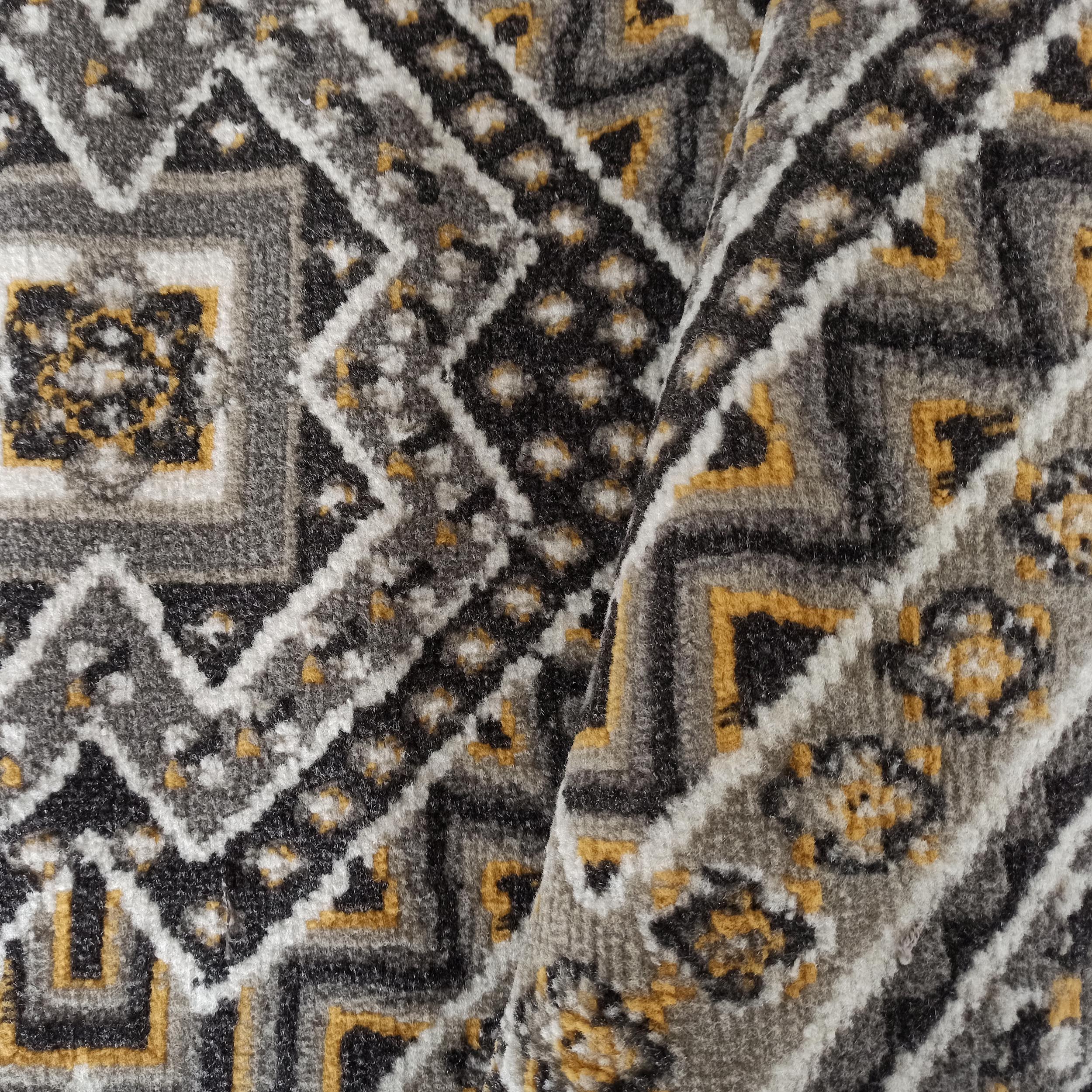 Tapis aux motifs géométriques complexes en noir, blanc, gris et jaune ocre, avec une texture douce et bouclée