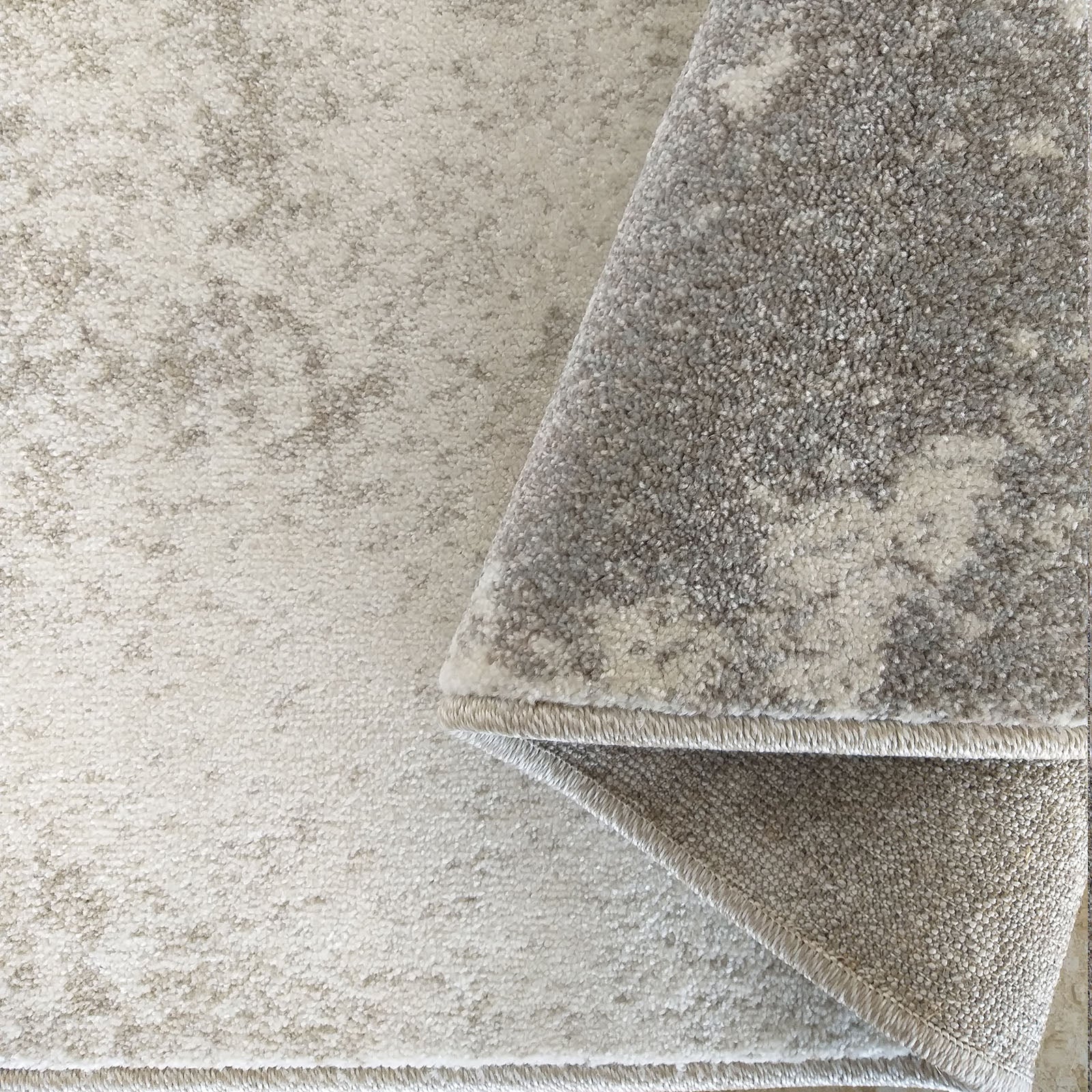 Gros plan d'un tapis beige clair à motifs abstraits gris délavés, partiellement roulé sur lui-même