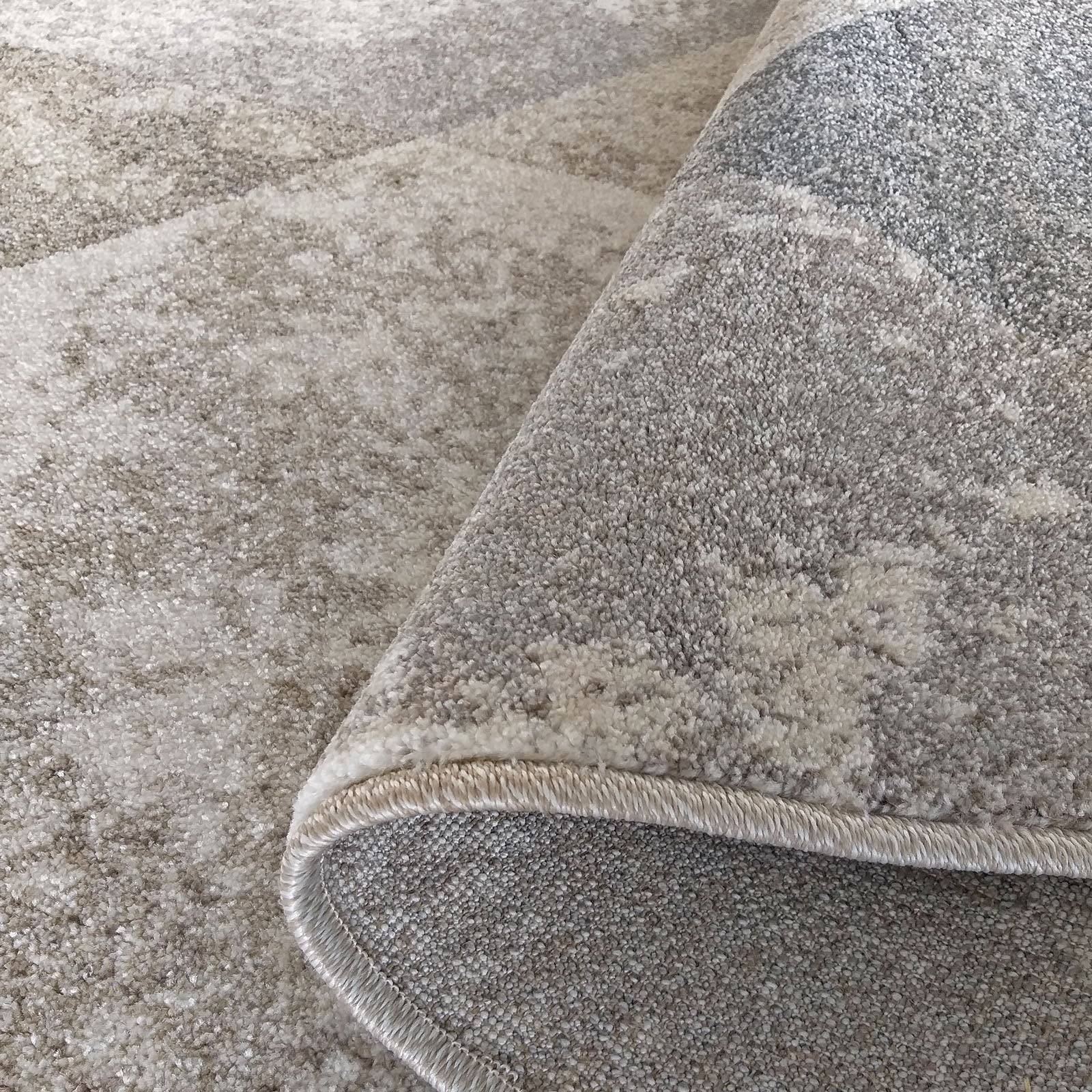 Tapis à poils longs et texture douce en nuances de beige et de gris clair, roulé pour montrer son envers et ses bordures